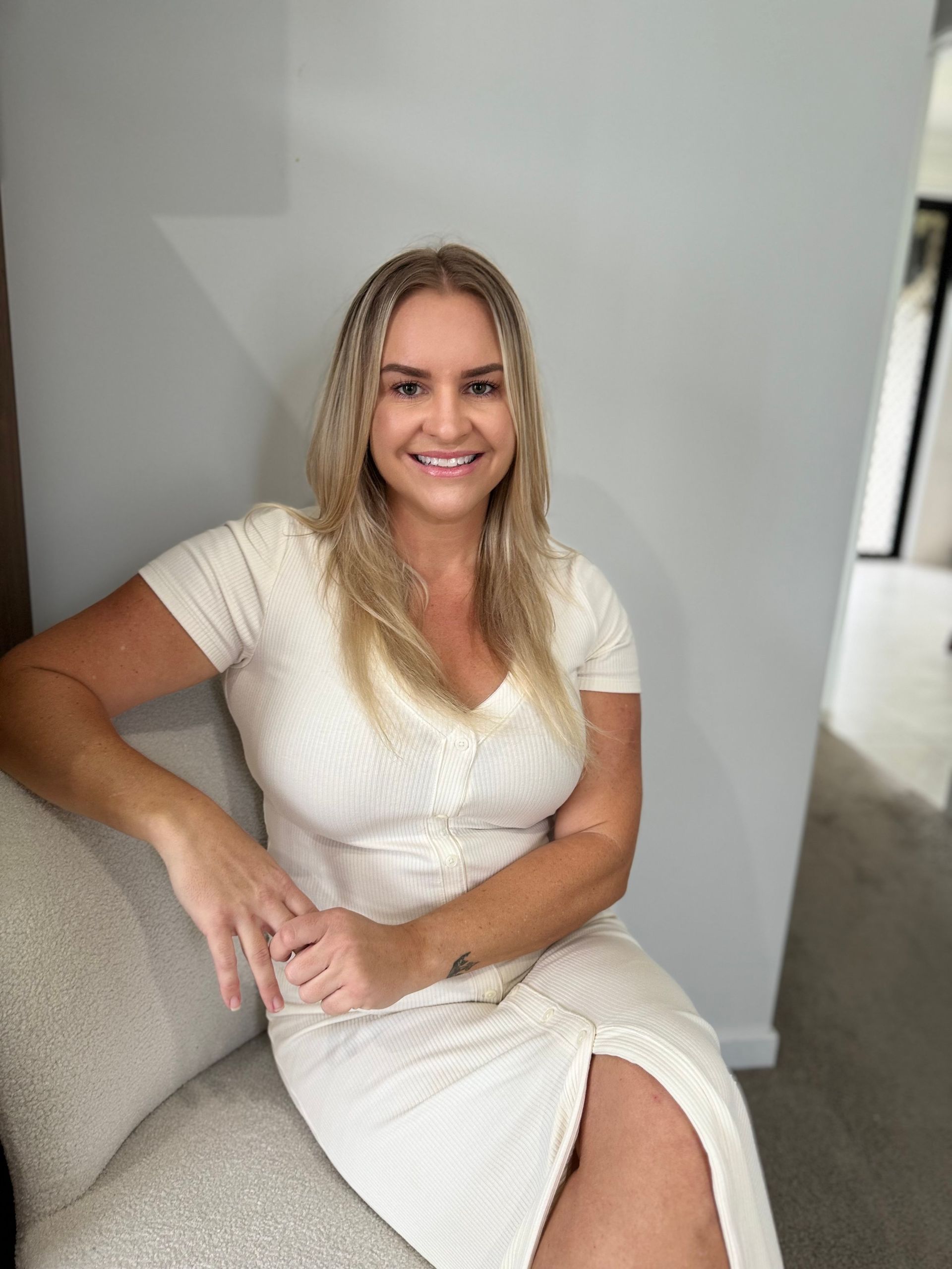 Woman With Blonde Hair Smiles, Wearing a Cream-colored Dress — Skin Haven Aesthetics Whitsundays in Airlie Beach, QLD