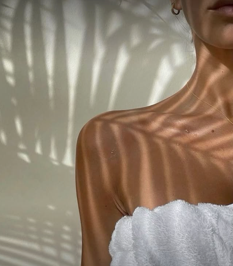 Shoulder and neck bathed in sunlight, with palm tree shadow patterns on a white wall.— Skin Haven Aesthetics Whitsundays in Airlie Beach, QLD