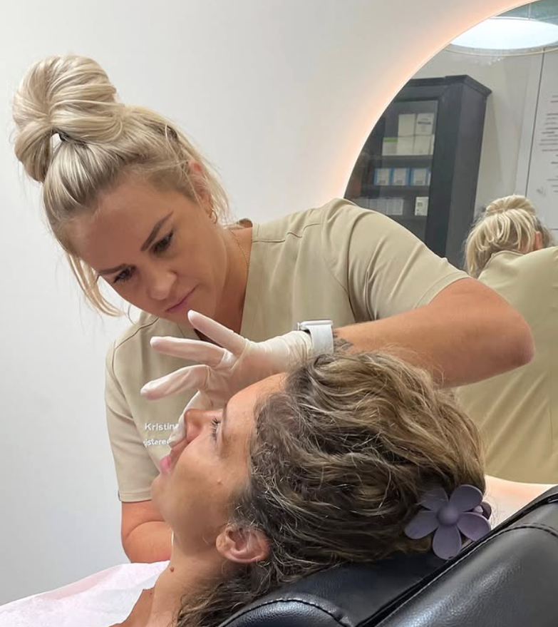Woman in gloves examines patient's face in clinic, reflection in mirror visible.— Skin Haven Aesthetics Whitsundays in Airlie Beach, QLD