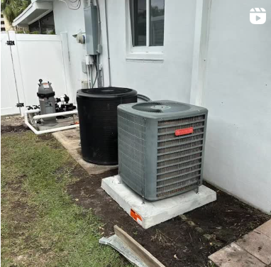 A gray air conditioner is sitting on top of a concrete platform in the backyard of a house.