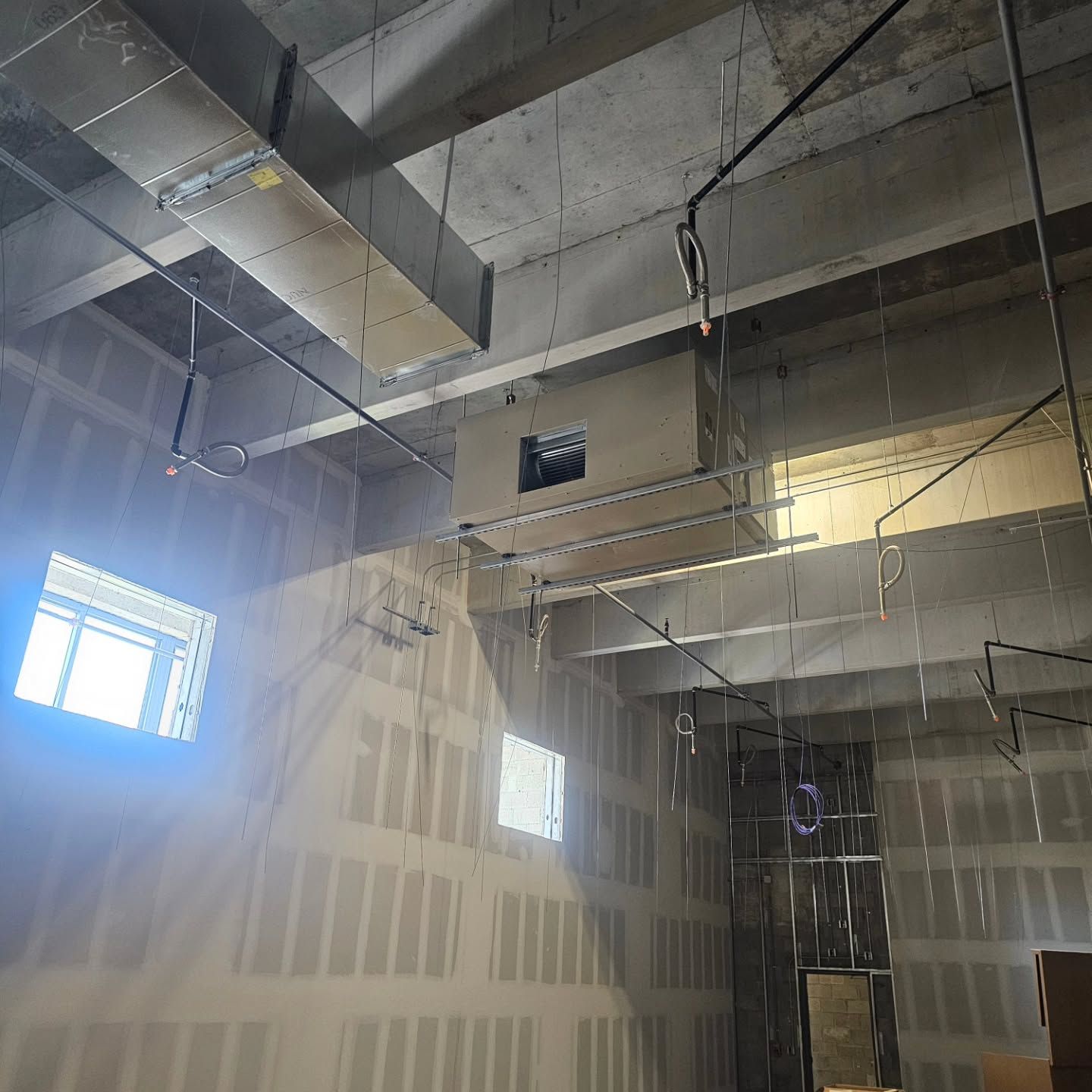 A room with a lot of ducts hanging from the ceiling and a window.