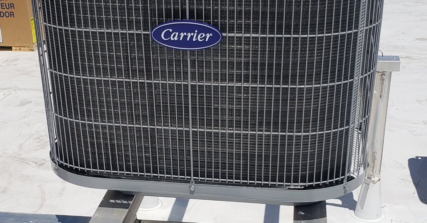 A carrier air conditioner is sitting on top of a white roof.