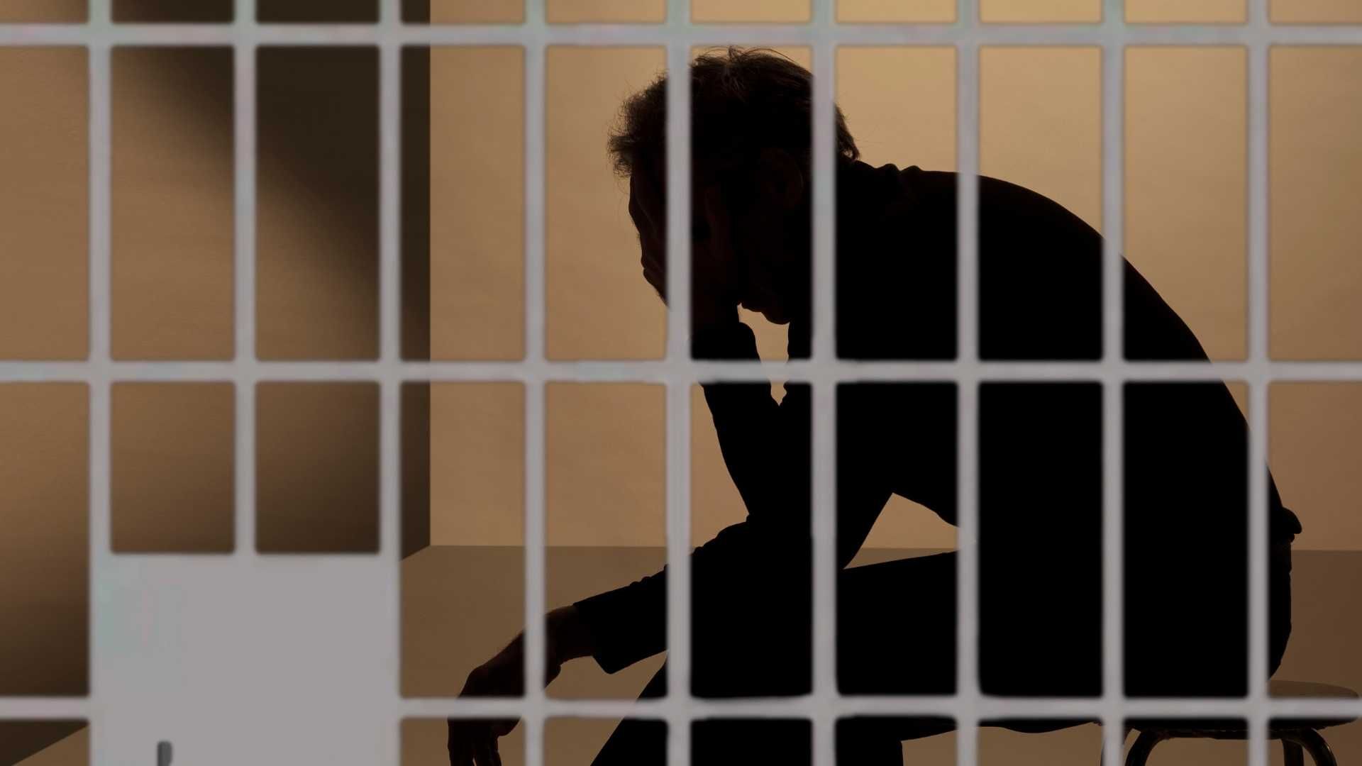 prisoner sitting in a prison cell with his hand covering his face