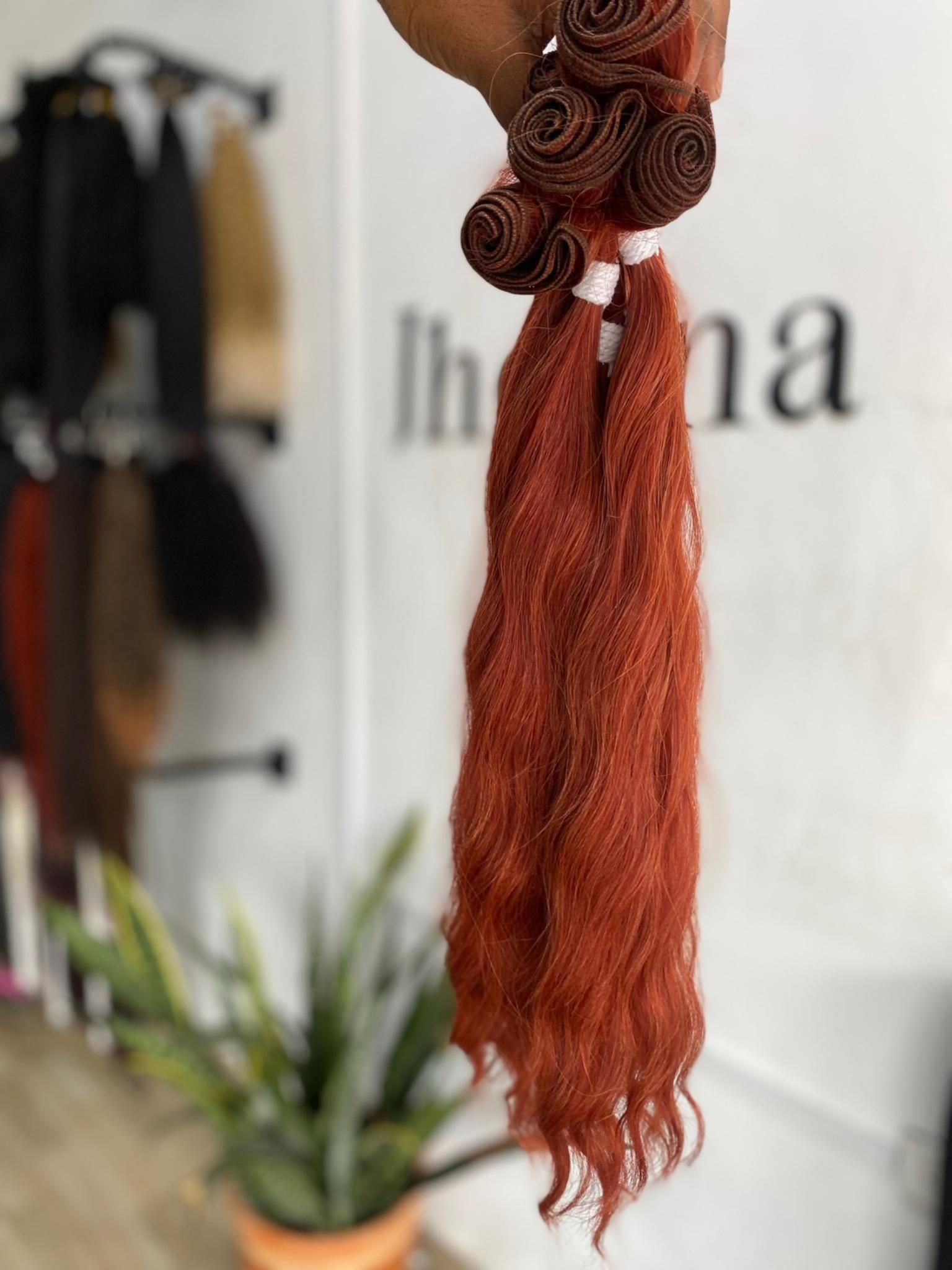 Una persona sostiene un mechón de extensiones de cabello texturizadas de color cobre en un salón de belleza.