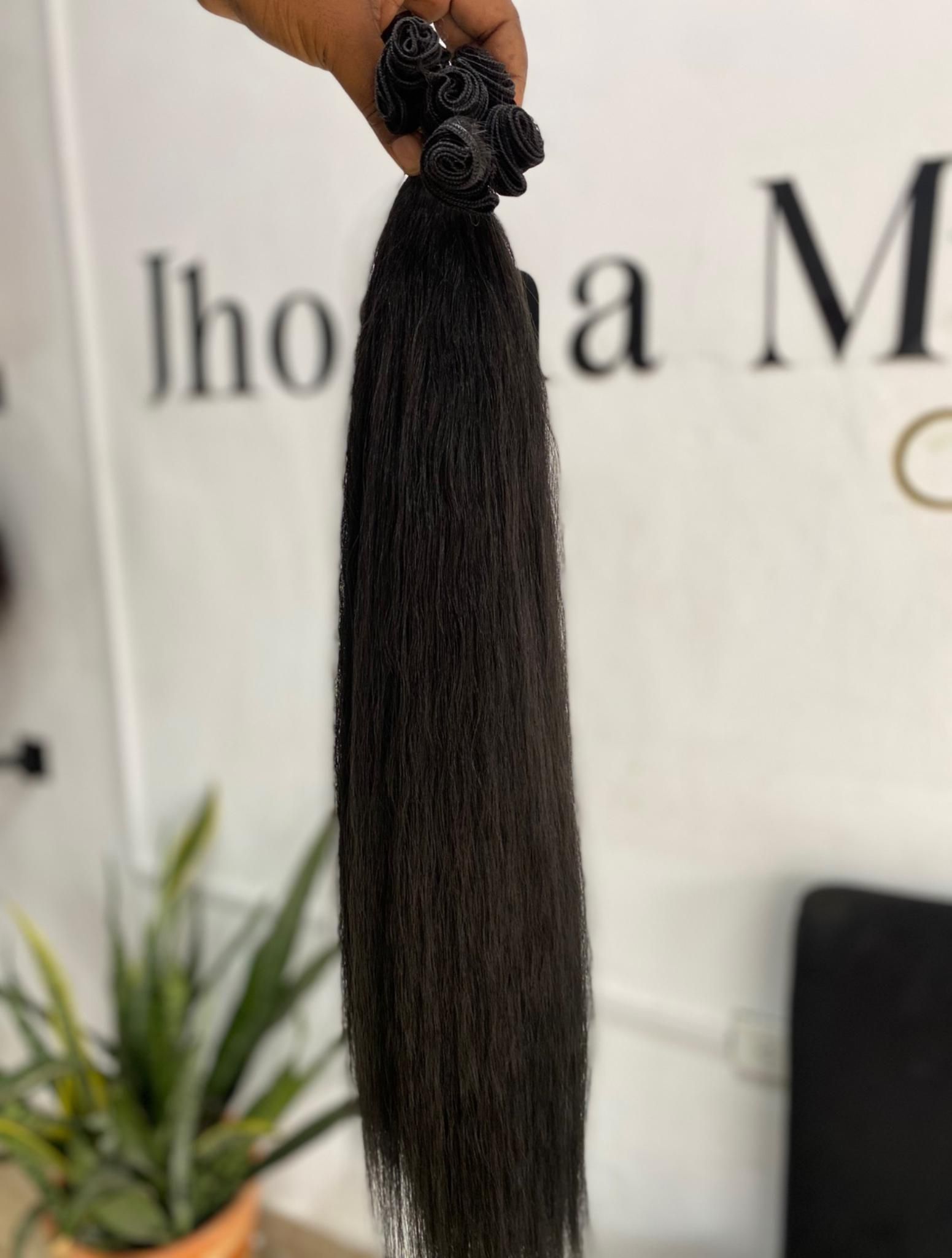 Una mano sostiene un largo mechón de extensiones de cabello rizado y texturizado, de color marrón oscuro, contra una pared de color claro.