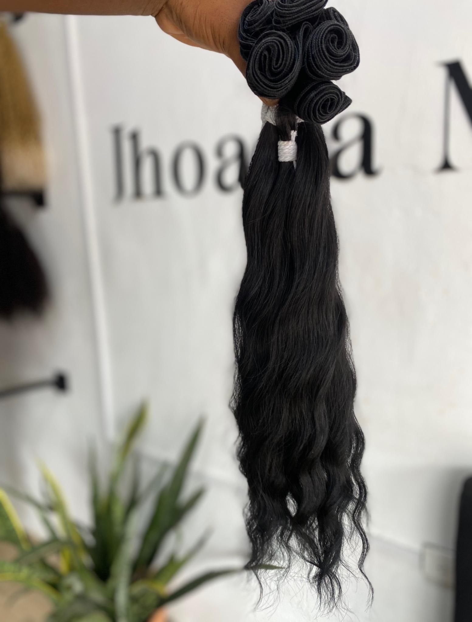 Una mano sostiene un manojo de extensiones de cabello negro y rizado sobre un fondo borroso con texto.