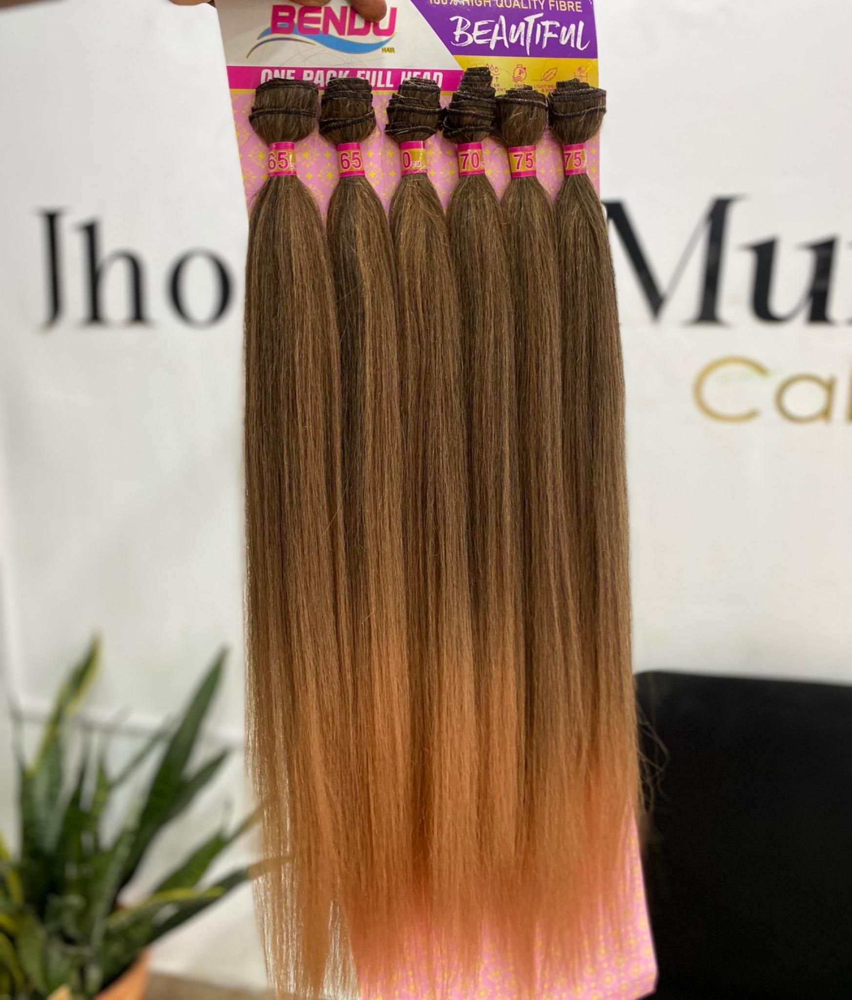 Una mano sostiene un paquete de seis extensiones de cabello con efecto degradado, que van desde el castaño en las raíces hasta un tono rubio dorado más claro.