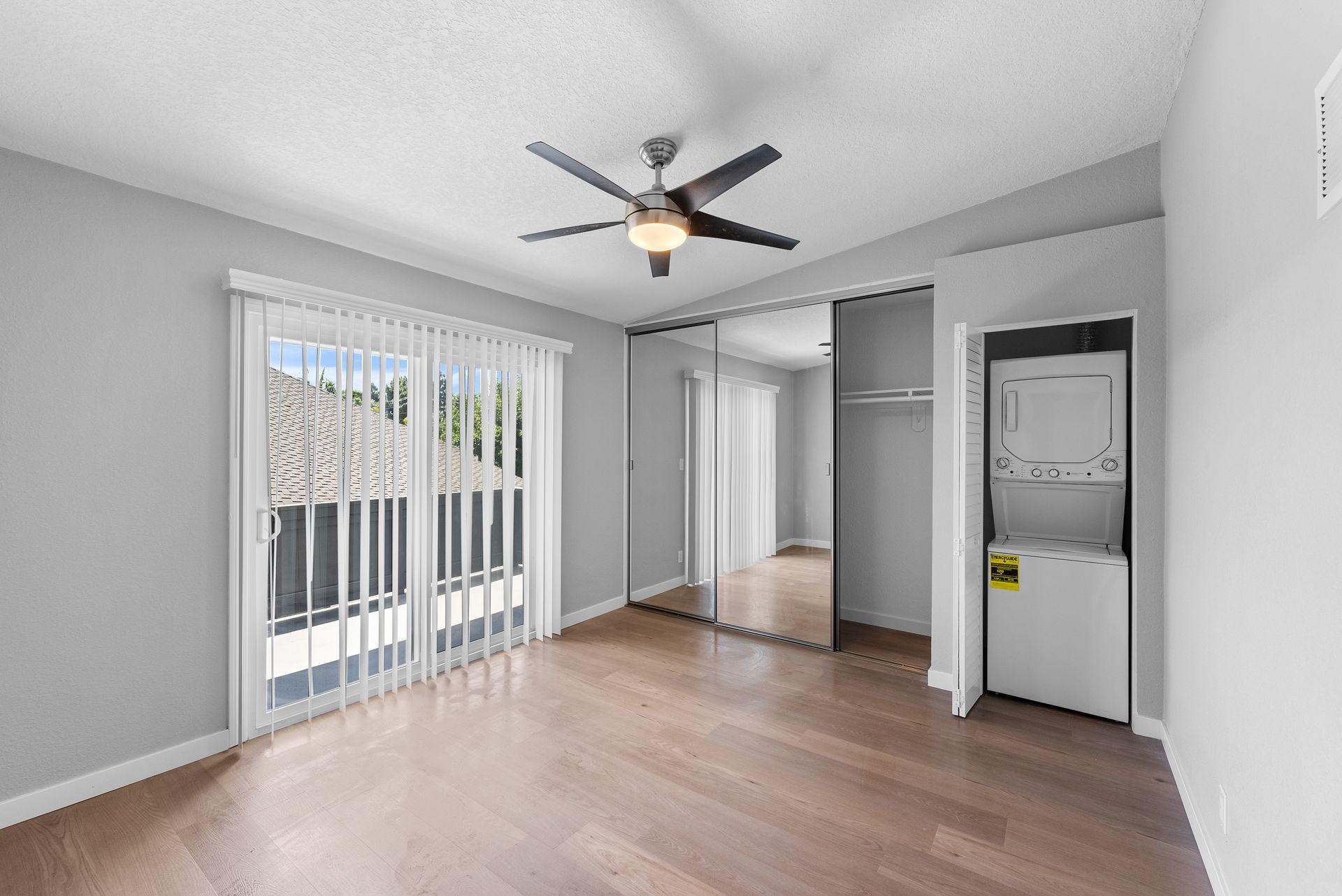 Wood floored bedroom with mirrored closet, sliding glass door and stacked washer and dryer