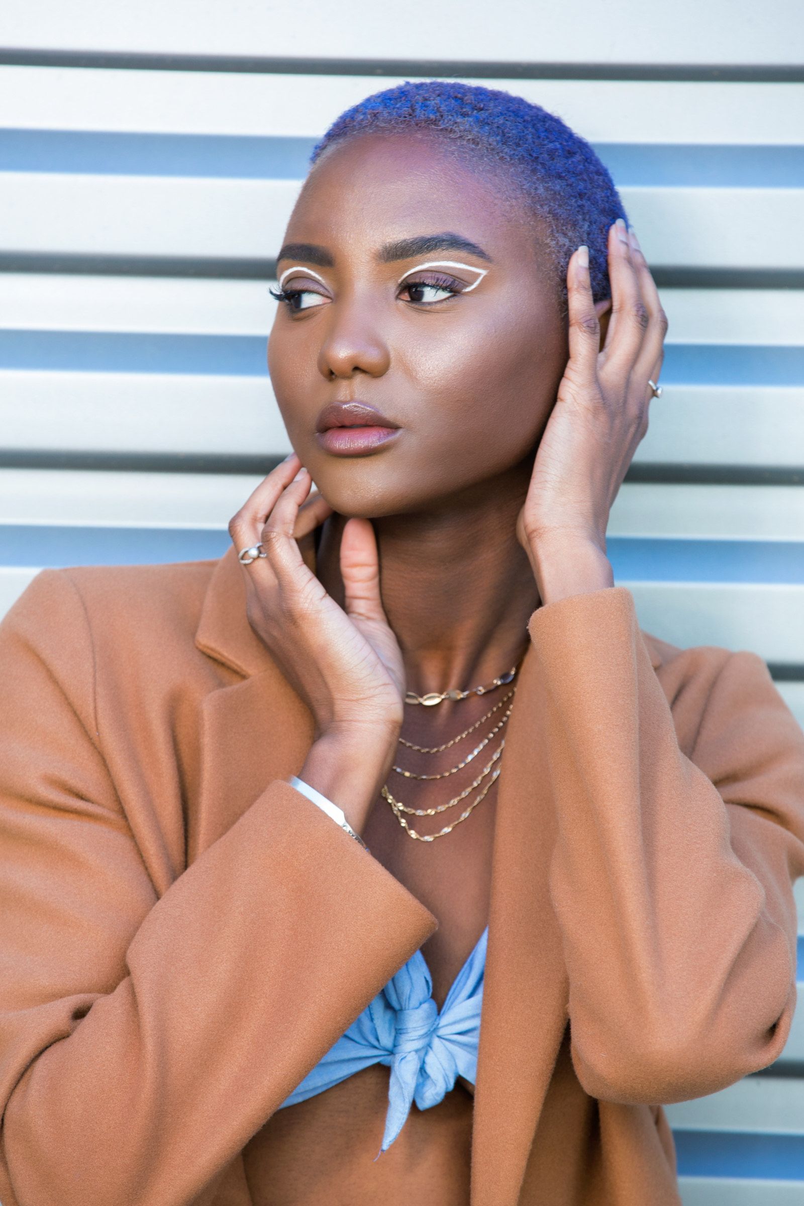 A woman with purple hair is wearing a brown jacket and a blue bikini top.
