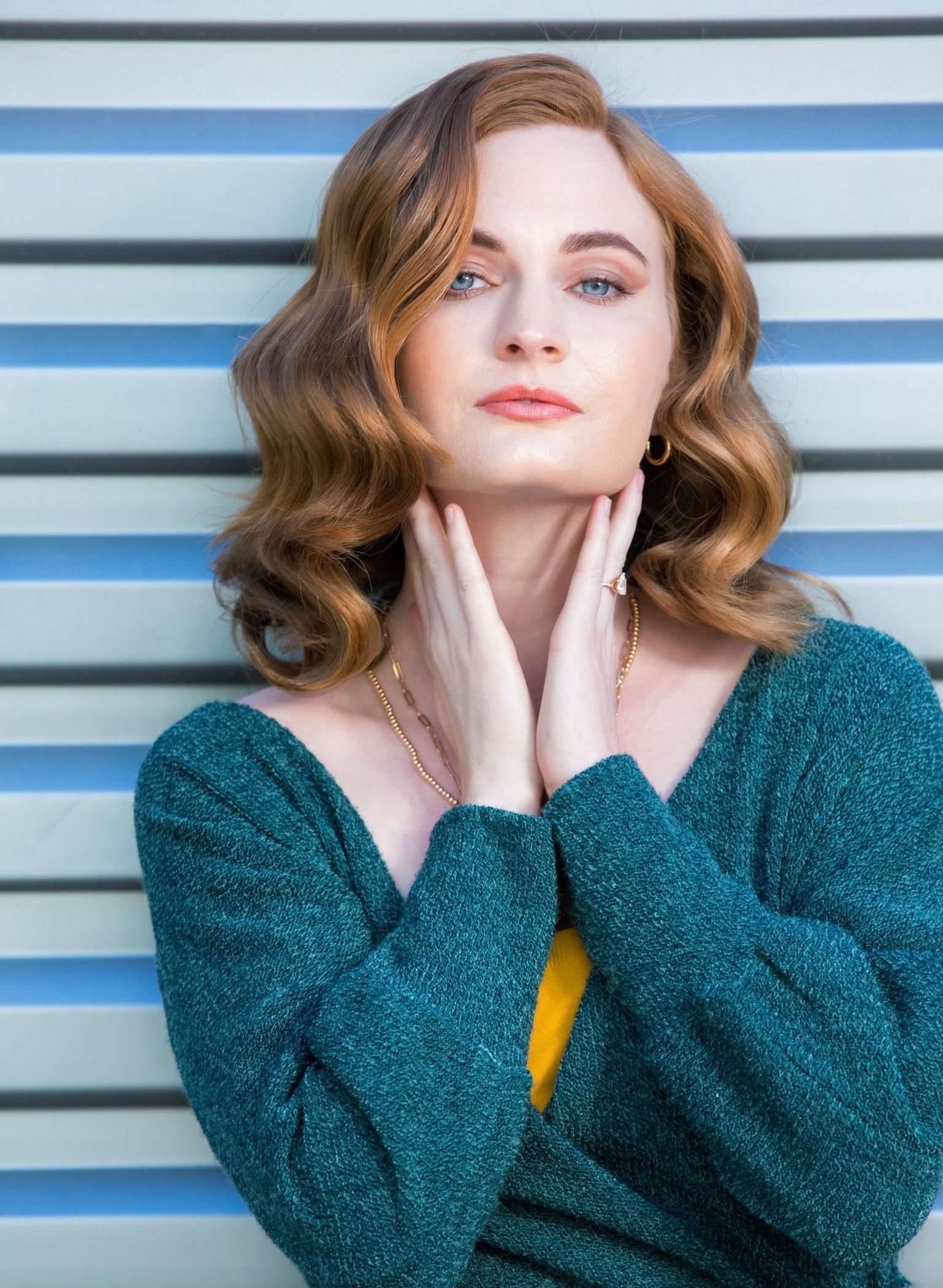A woman in a green sweater is standing in front of a striped wall.