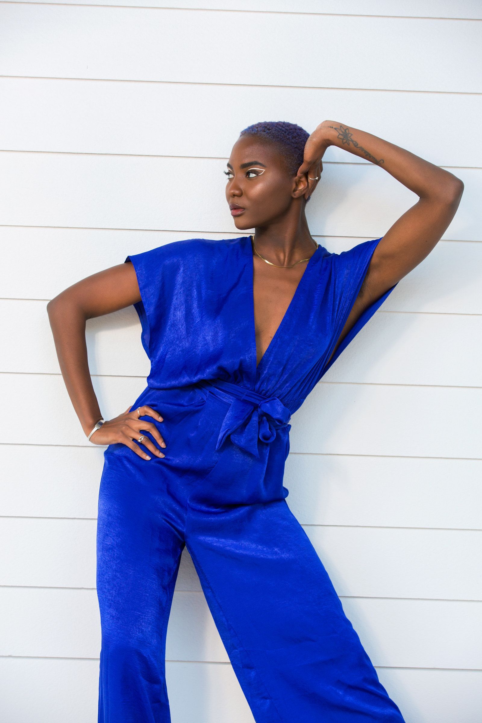 A woman in a blue jumpsuit is standing in front of a white wall.