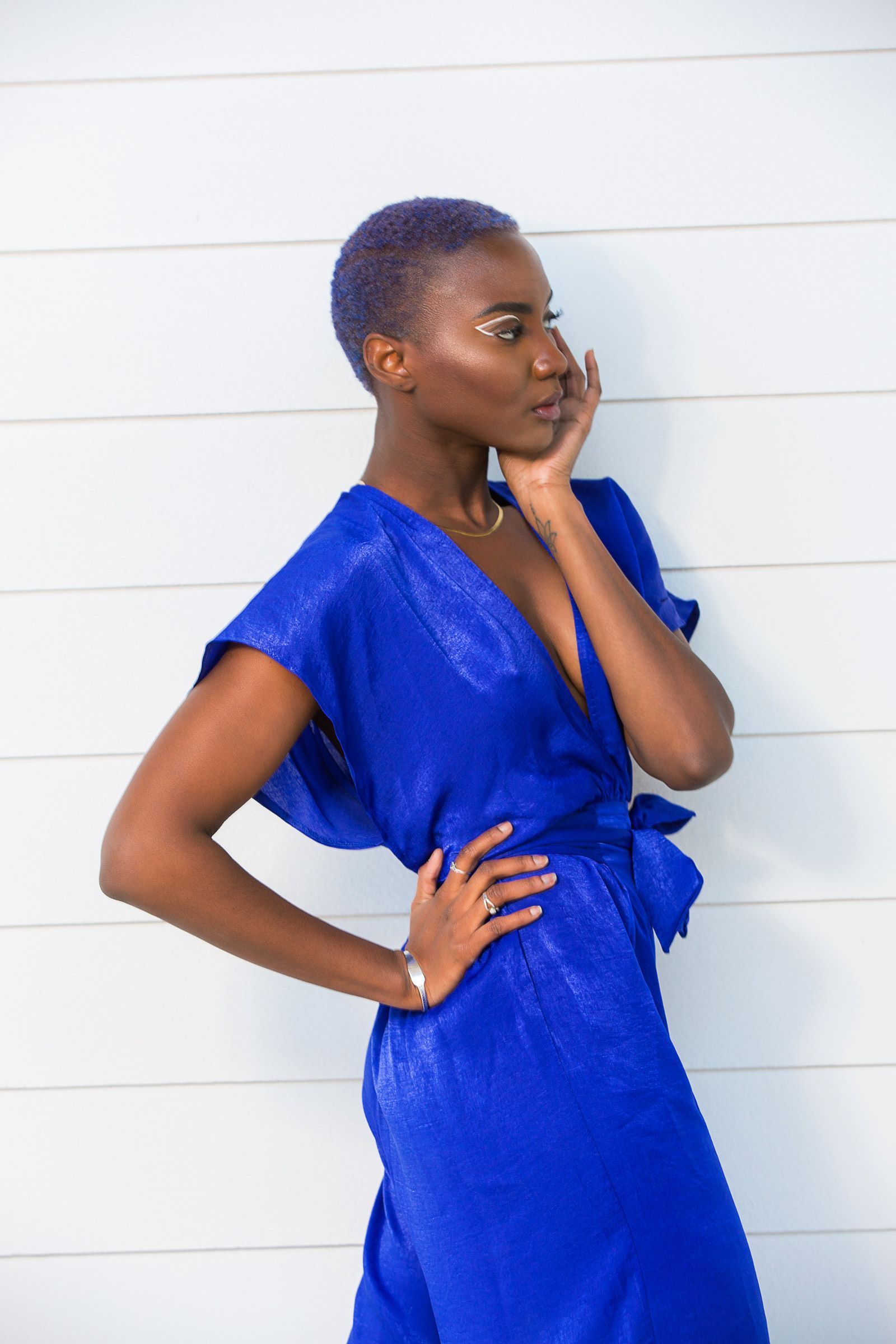 A woman in a blue dress is standing in front of a white wall.