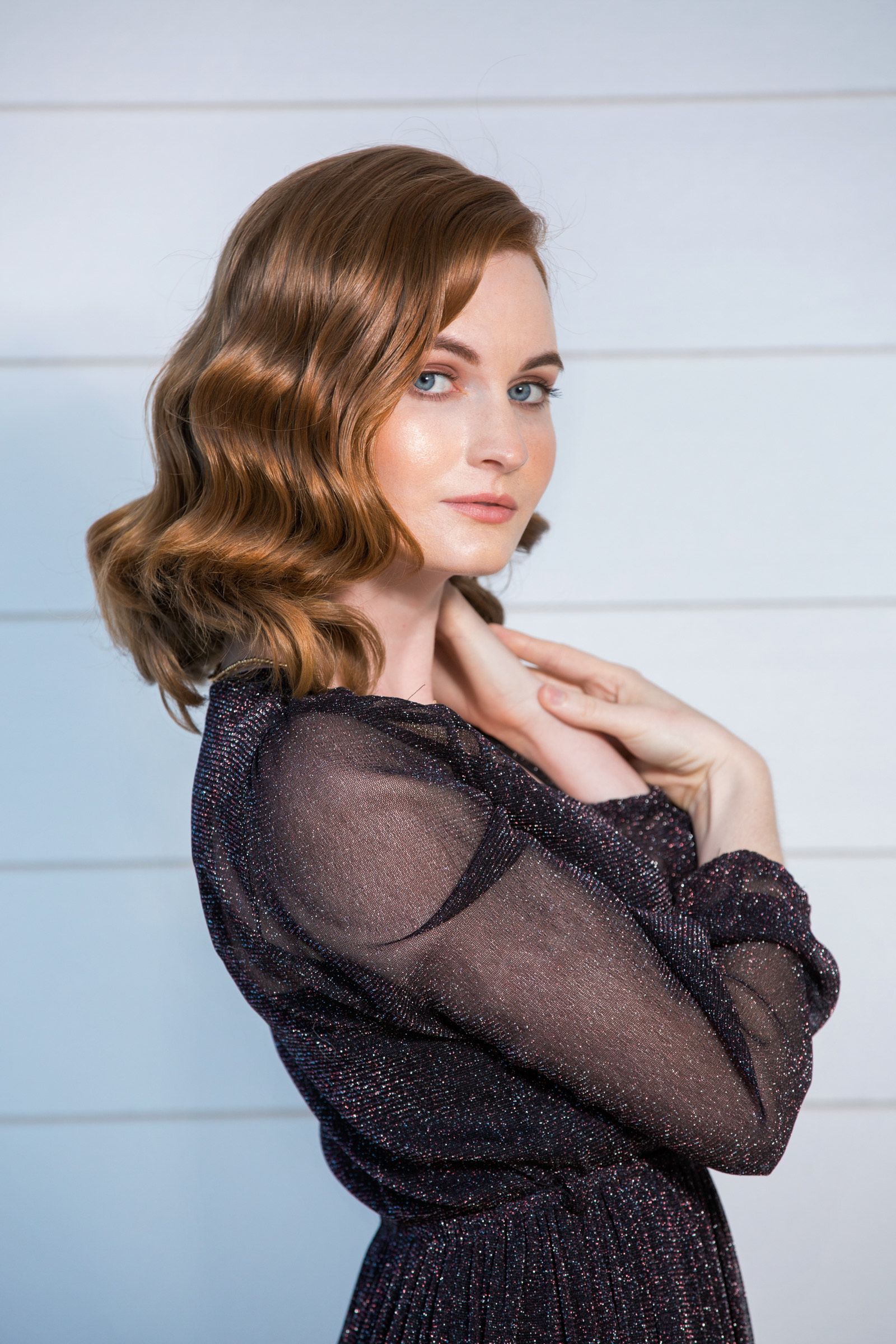 A woman in a black dress is standing in front of a white wall.