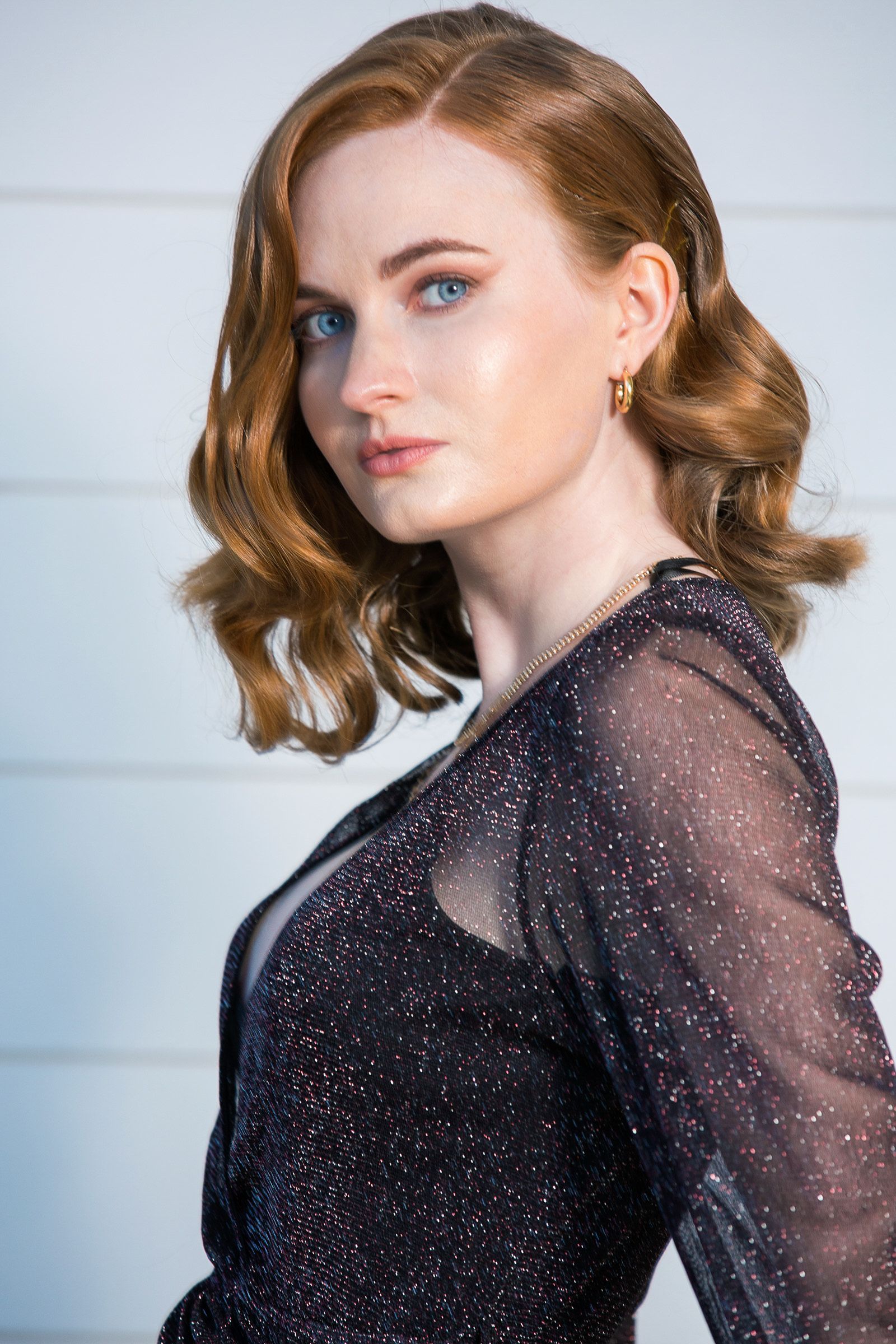 A woman with red hair is wearing a black dress and earrings.