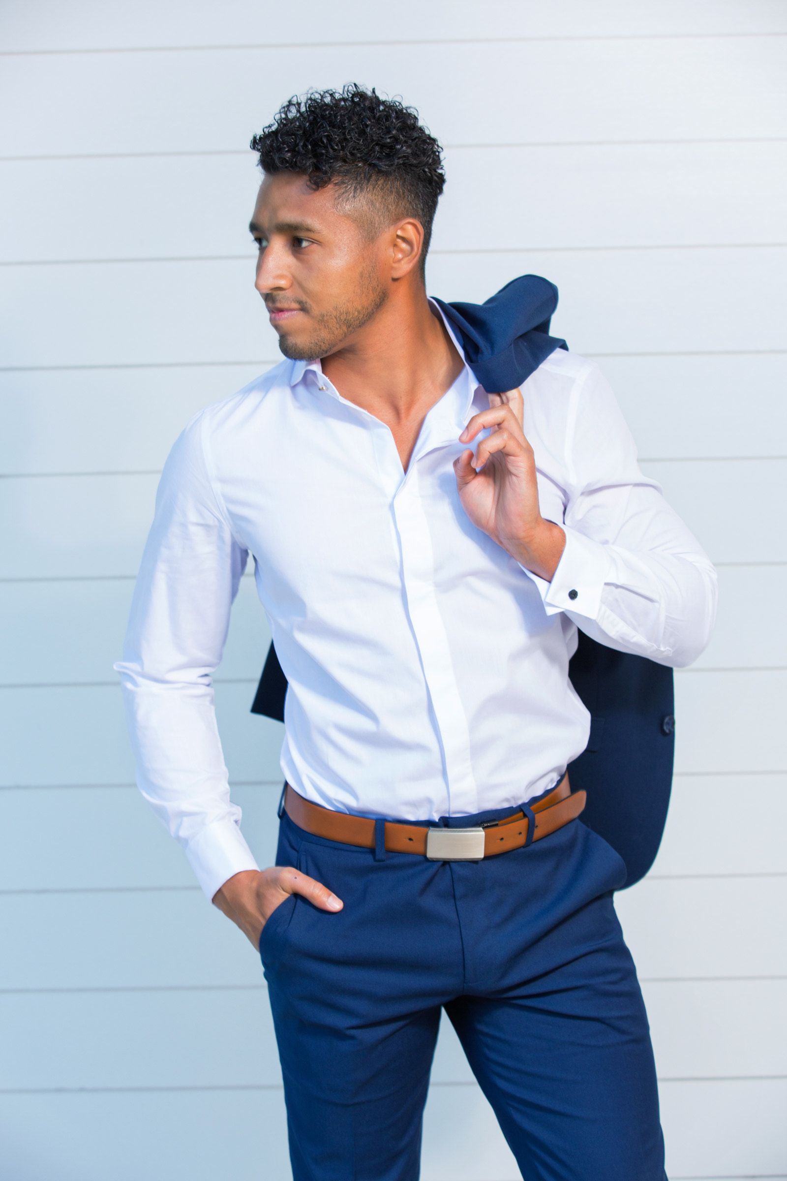 A man in a white shirt and blue pants is holding a jacket over his shoulder.