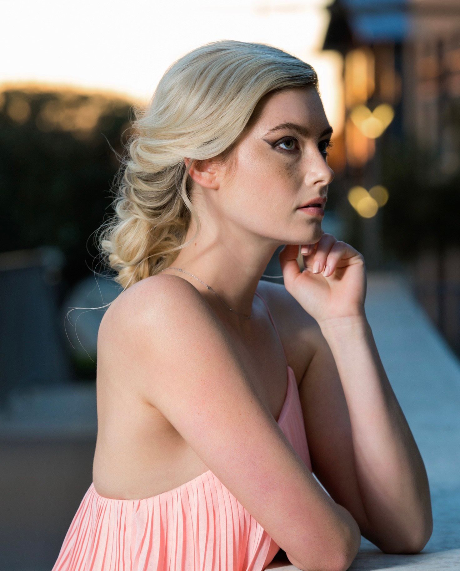 A woman in a pink dress is sitting on a bench with her hand on her chin.