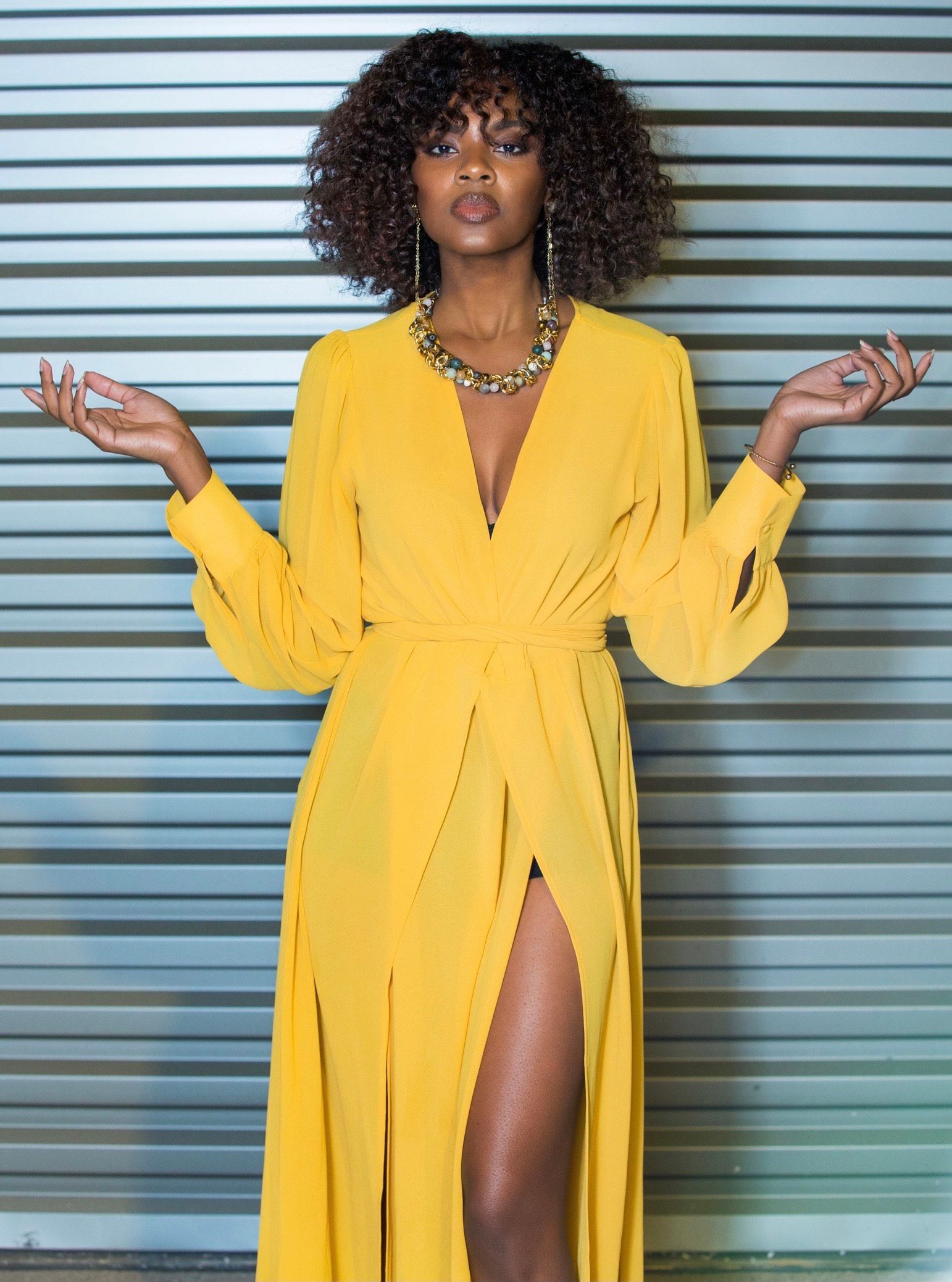 A woman in a yellow dress is standing in front of a metal wall.