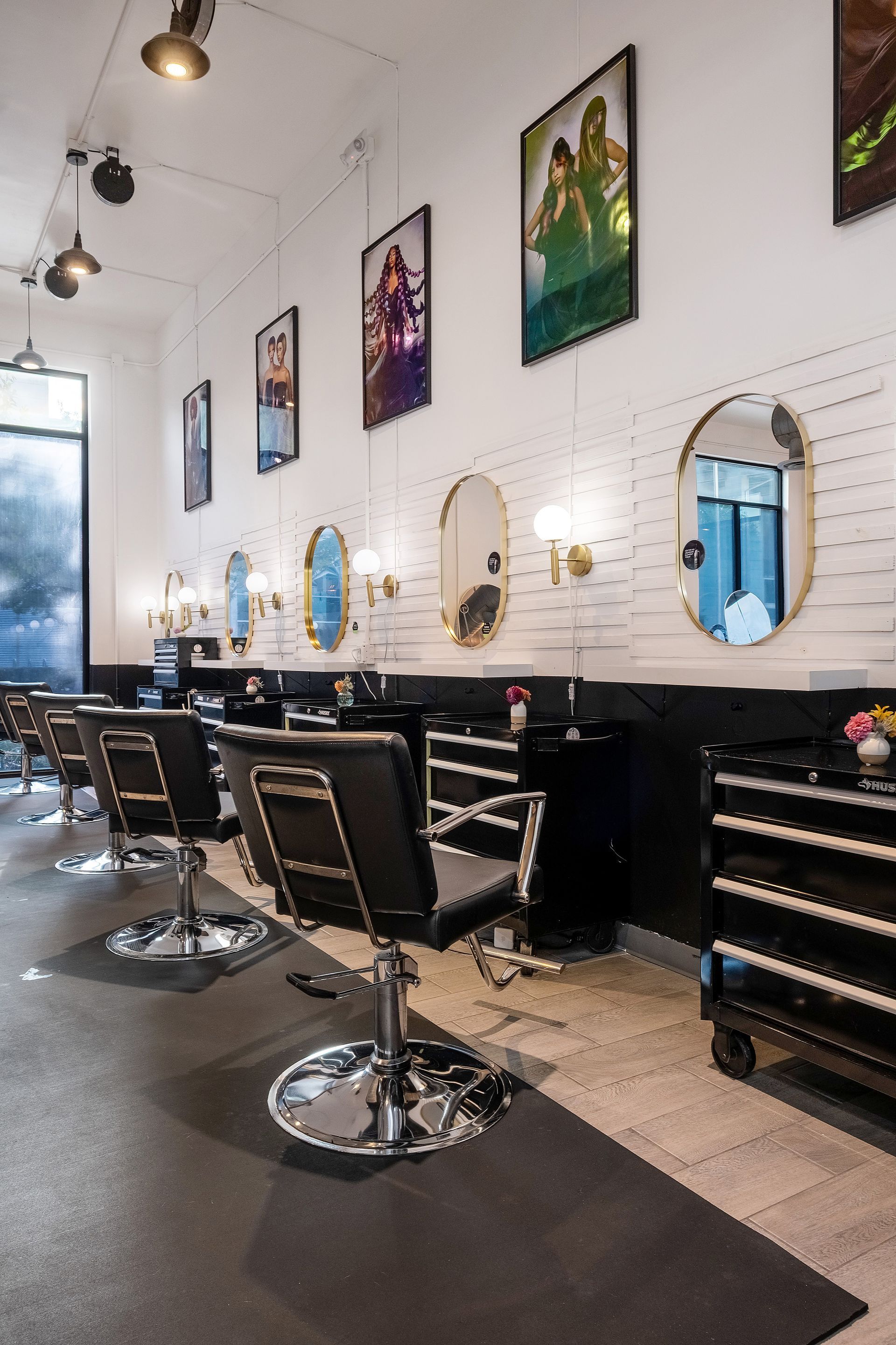 Hair salon with black chairs, oval mirrors, and artwork on white brick wall.