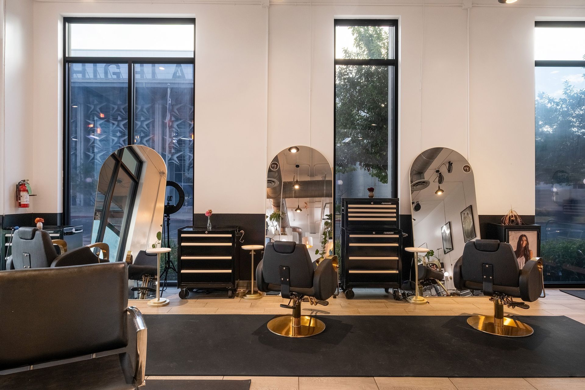 Hair salon interior with mirrors, chairs, and styling stations in front of large windows.