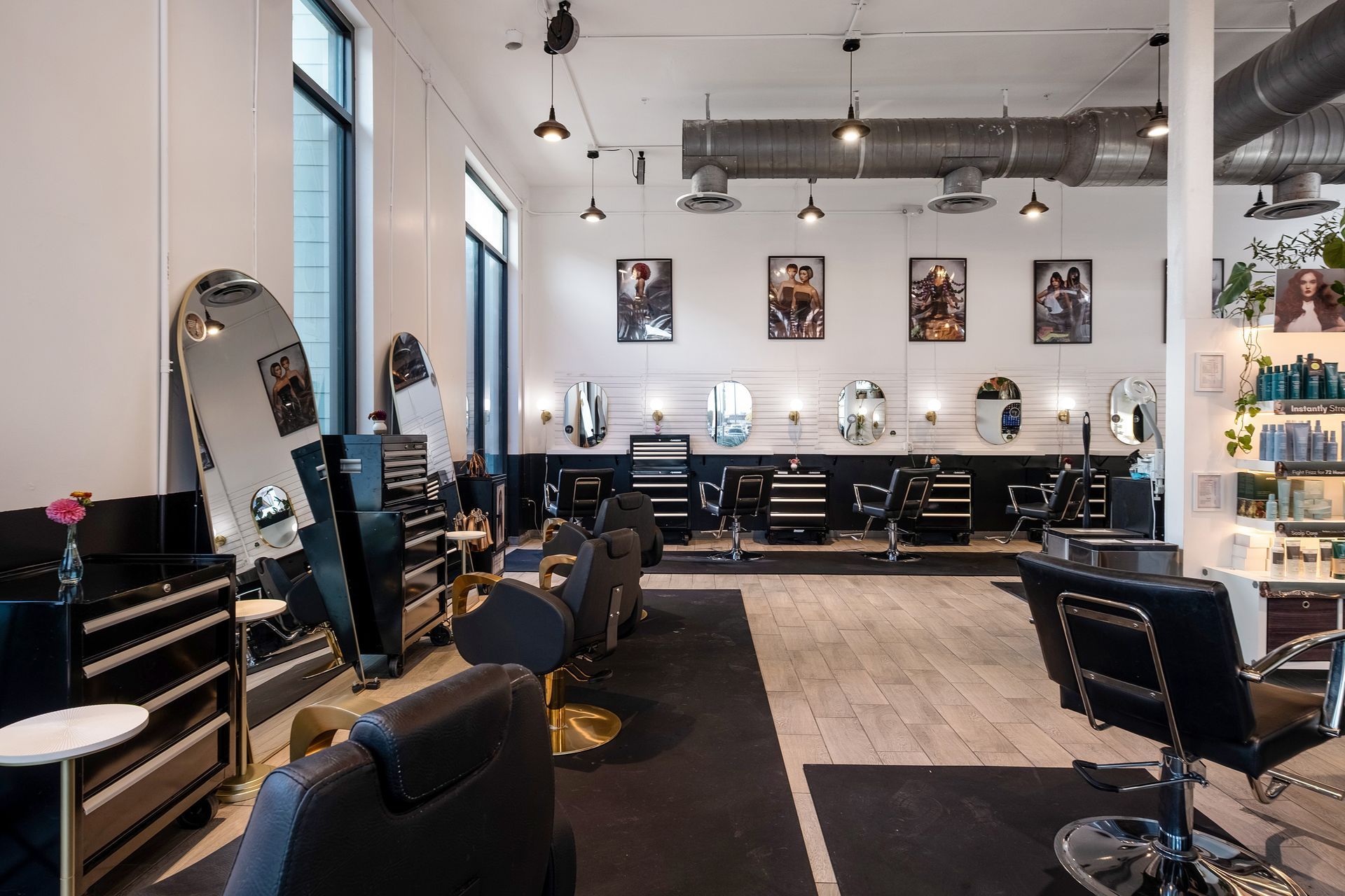 Hair salon interior with styling stations, mirrors, and chairs. White walls, black accents, and pendant lighting.