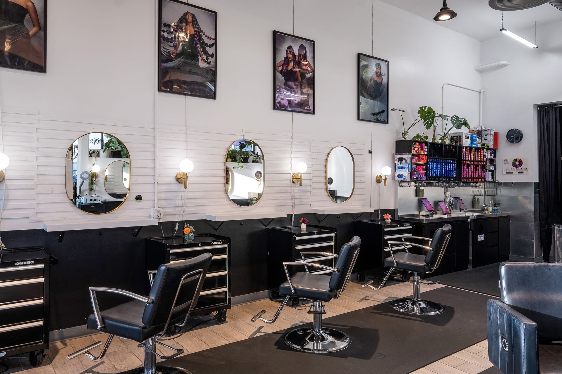 Hair salon interior with mirrors, chairs, and styling stations. White brick wall, black accents, and artwork.