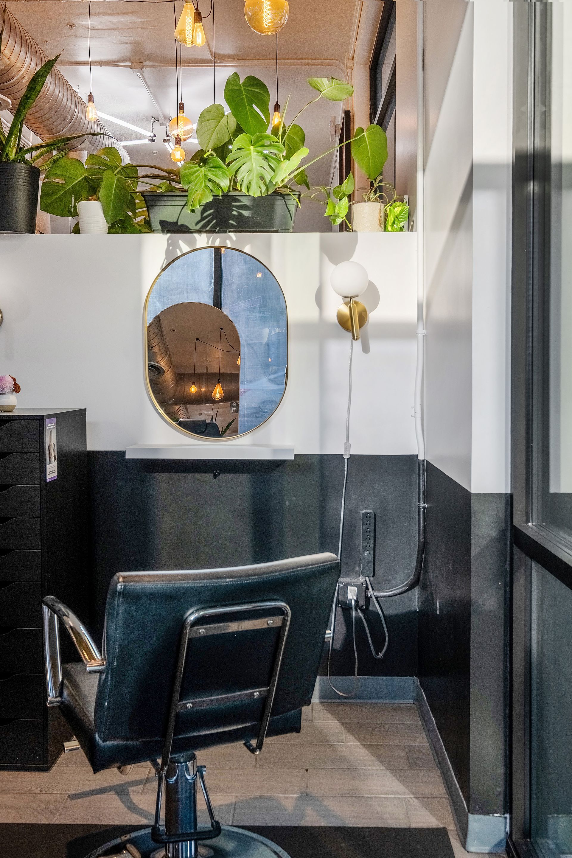 Hair salon interior with chair, mirror, plants, and black and white walls.