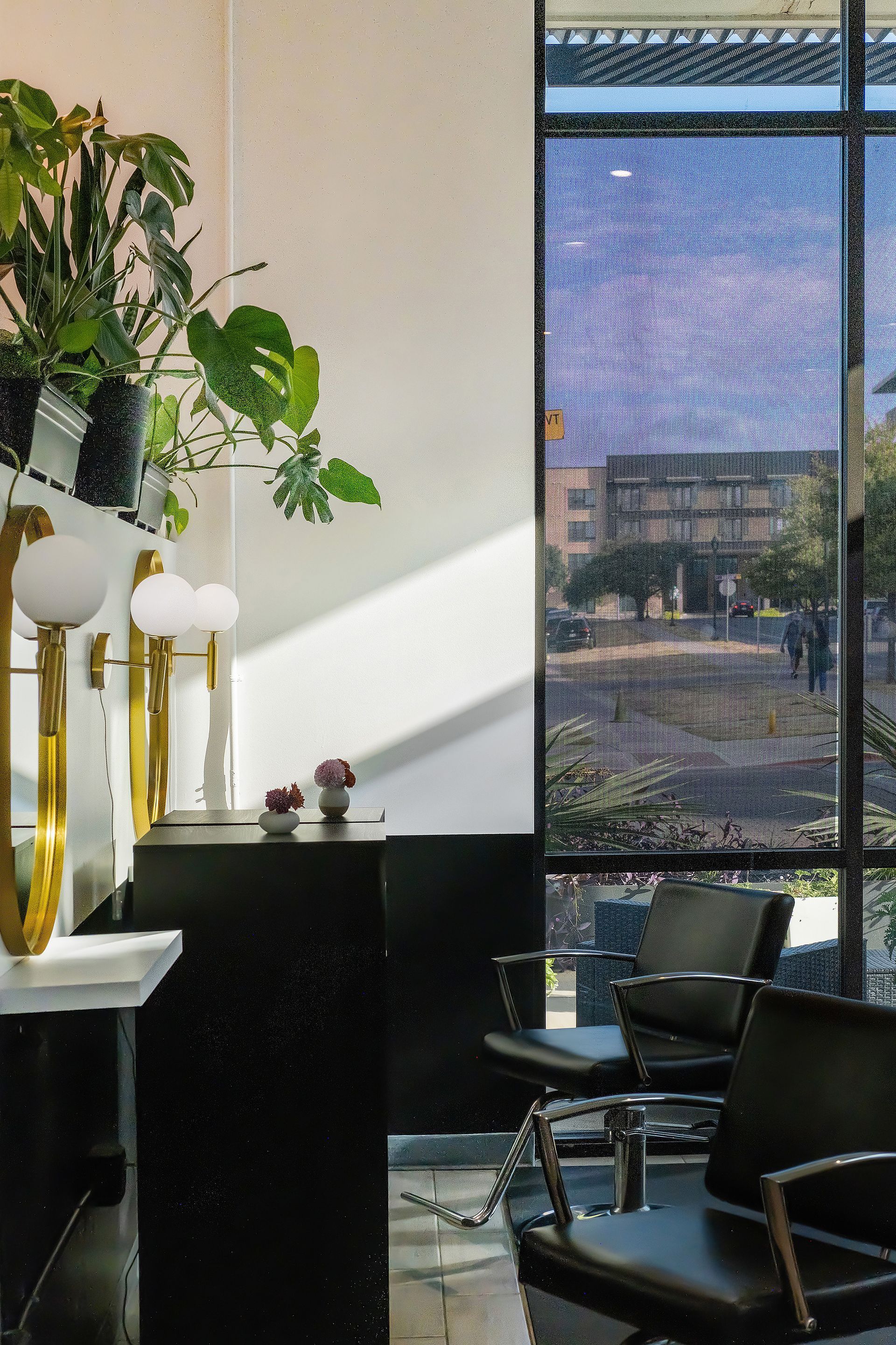 Hair salon interior with black and white decor, large window, plants, and chairs.