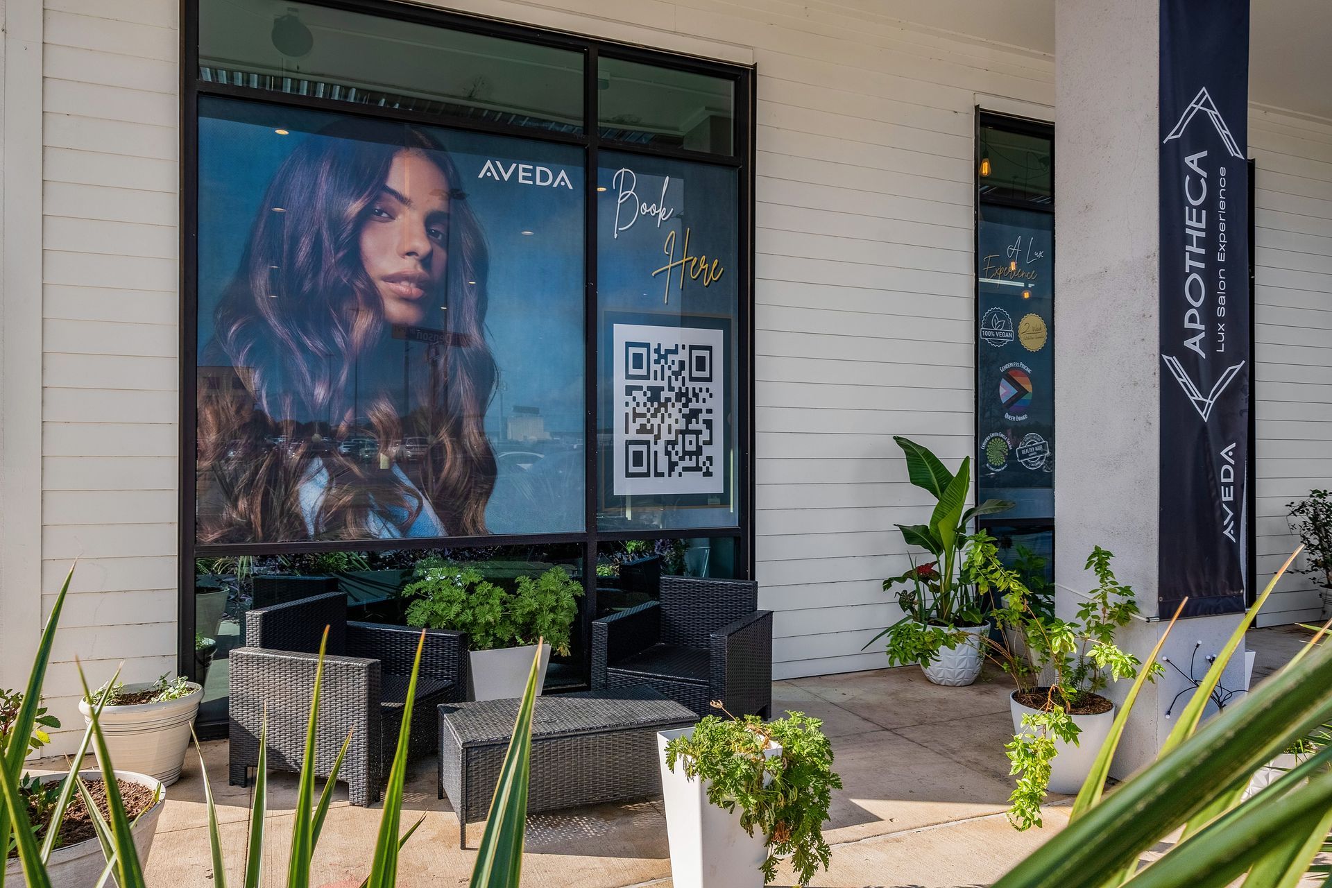 Exterior of an Aveda apothecary with a woman's portrait, a QR code, and outdoor seating.