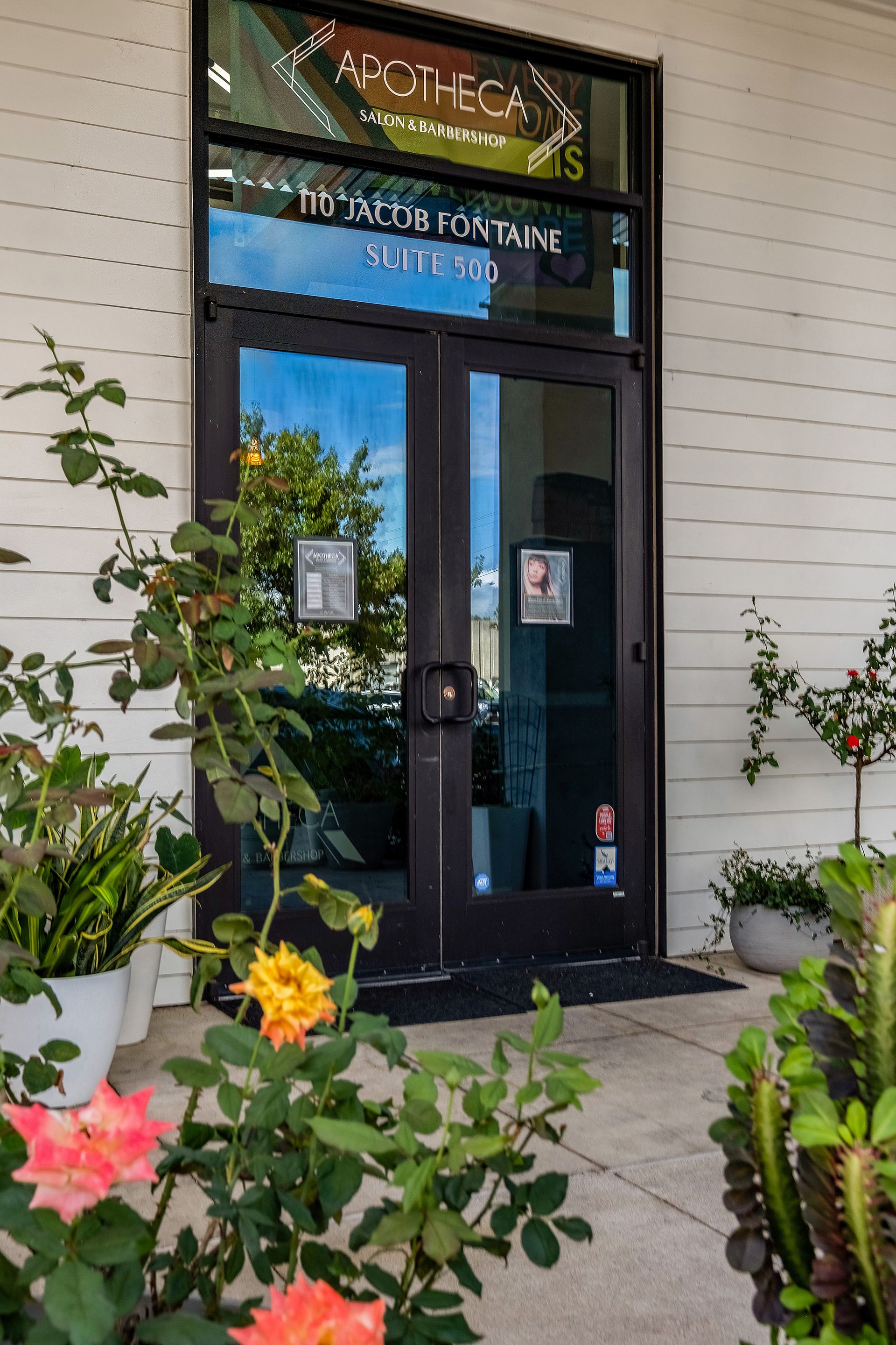 Entrance to Apotheca Wellness with double doors, plants, and signage in a white building.
