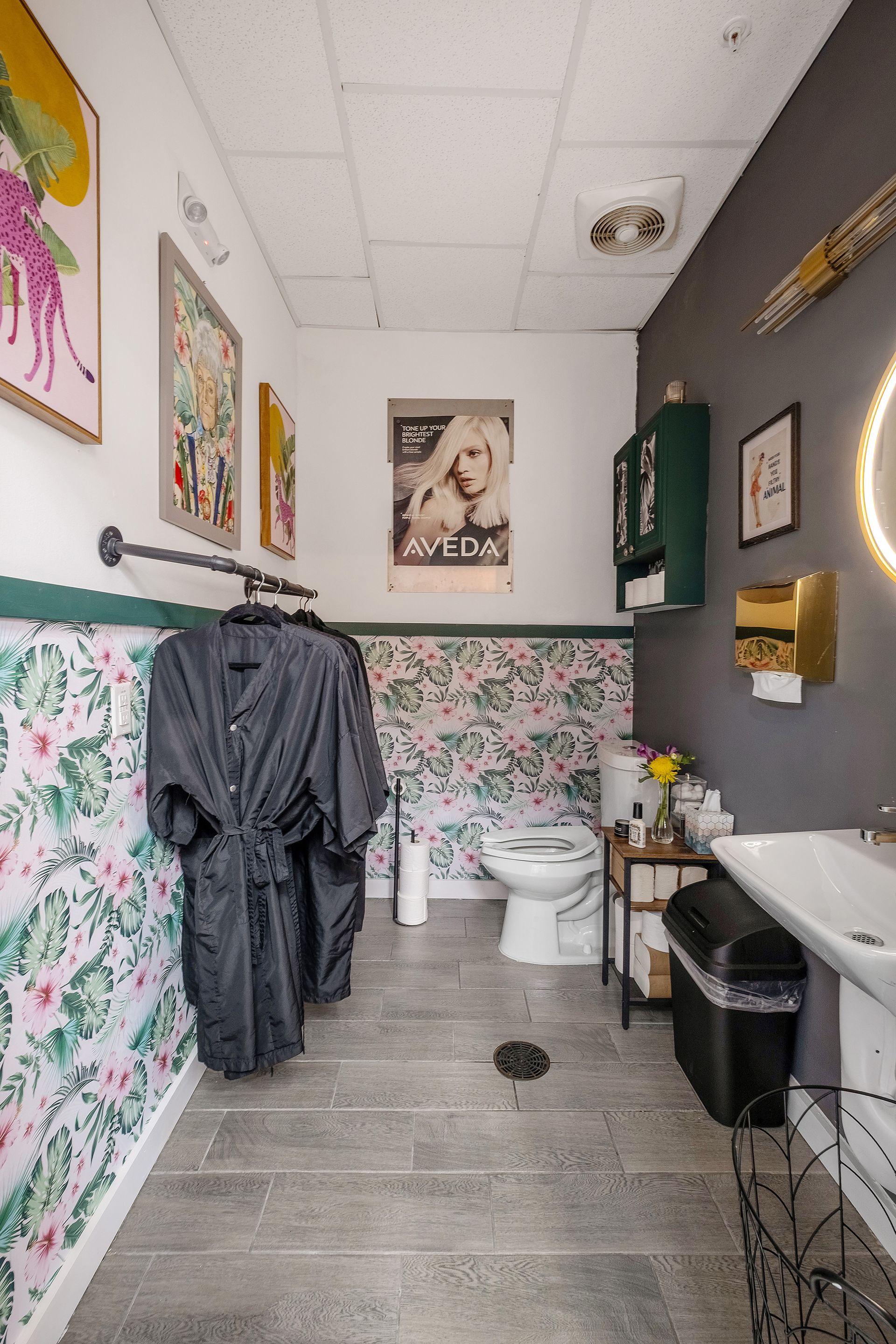 Bathroom with floral wallpaper, robes on a rack, toilet, and sink.