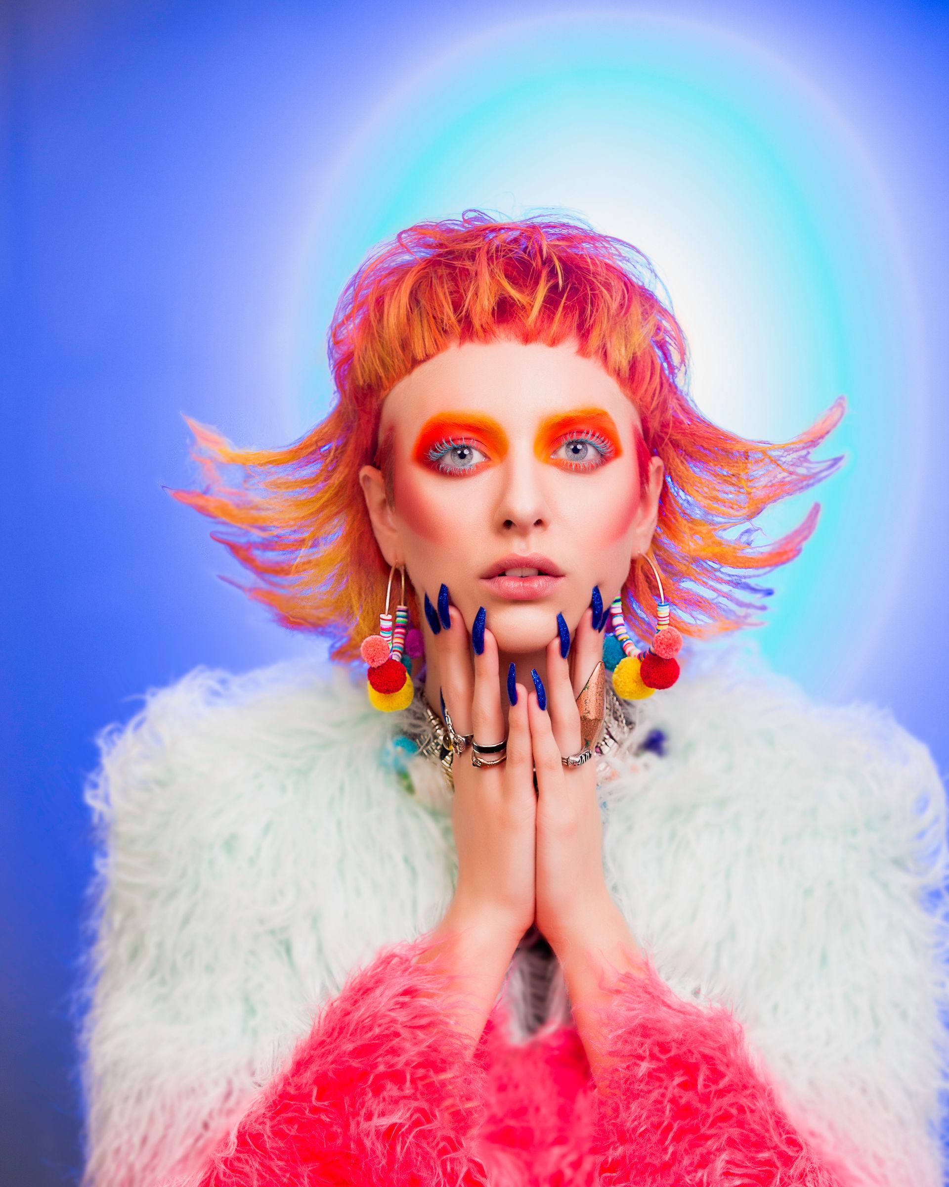 A woman with red hair and blue nails is wearing a fur coat and earrings.