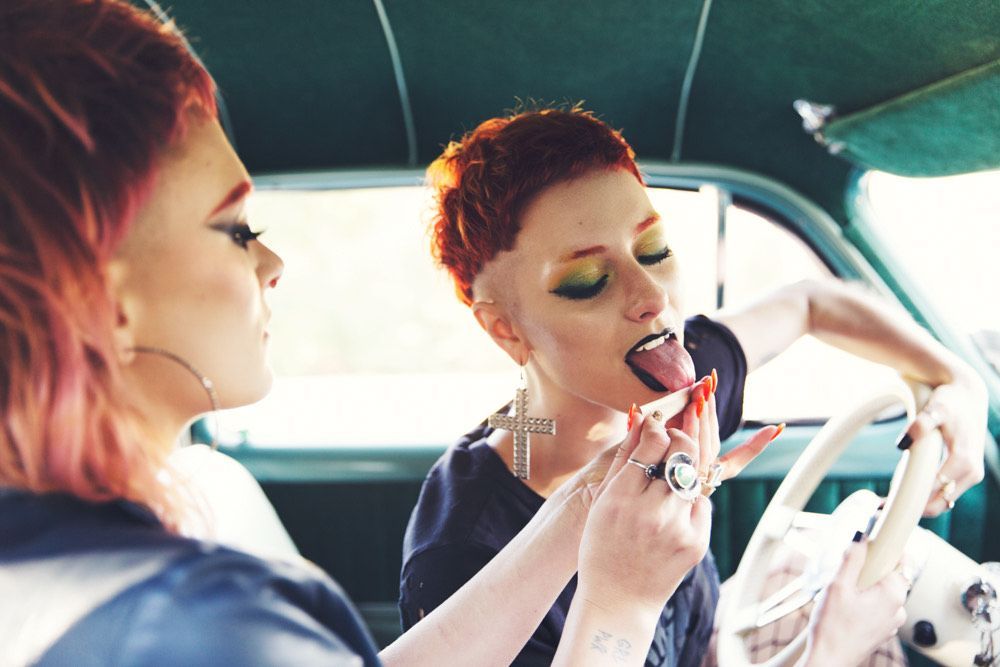 A woman is applying lipstick to another woman in a car.