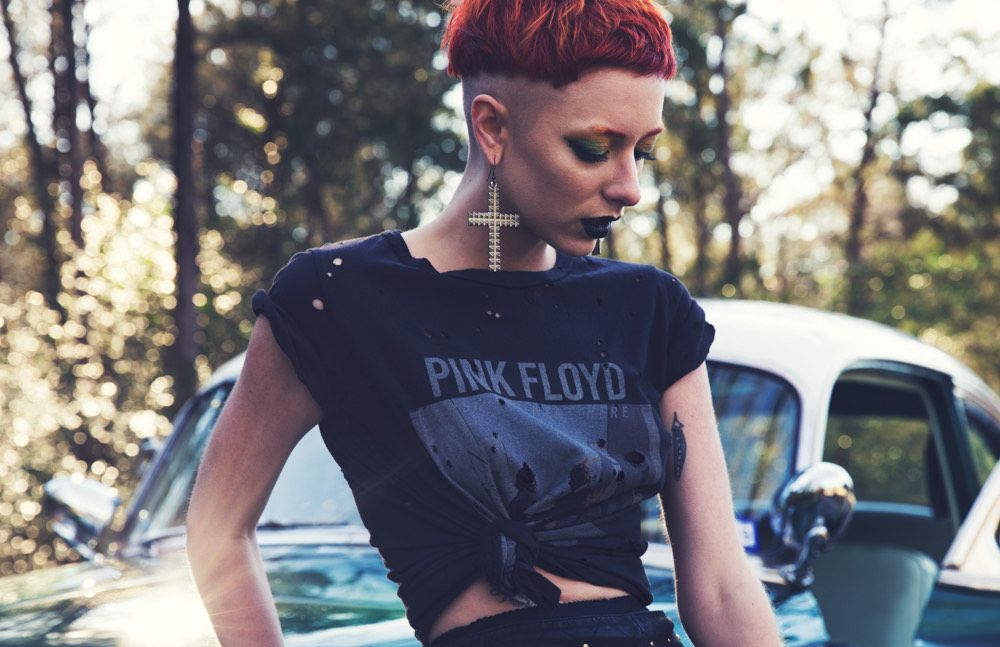 A woman wearing a pink floyd t-shirt is standing in front of a car.