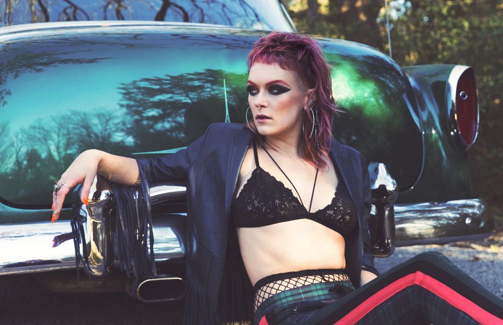 A woman with red hair is sitting next to a green car.