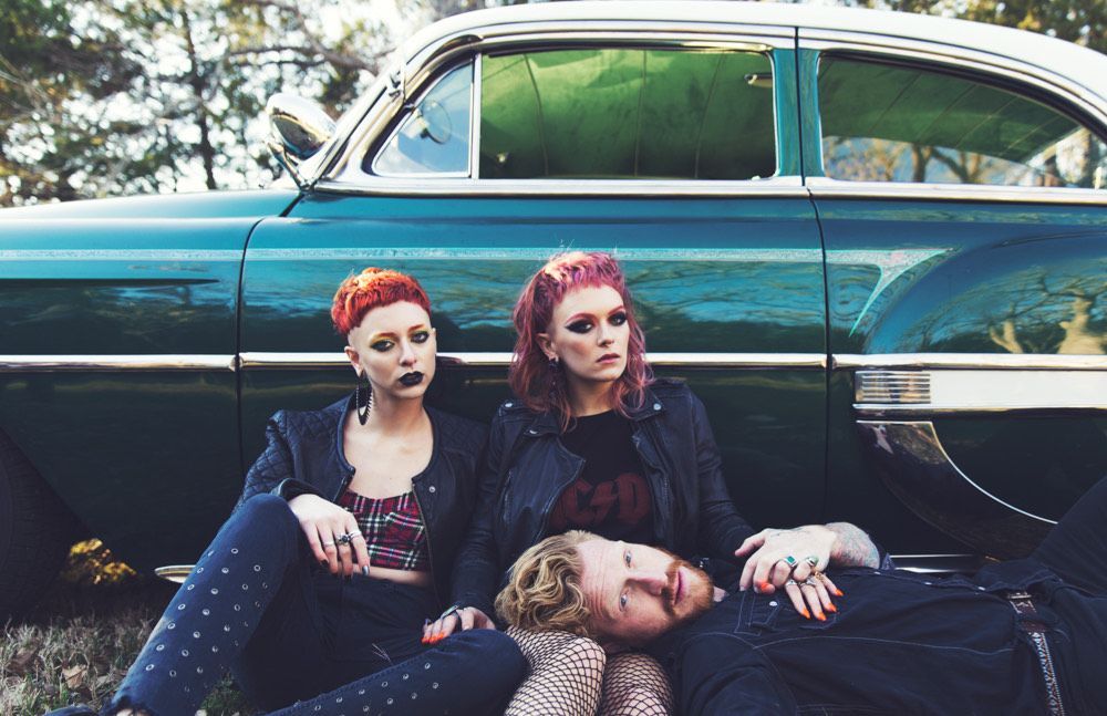 Three people are laying on the ground in front of a green car.