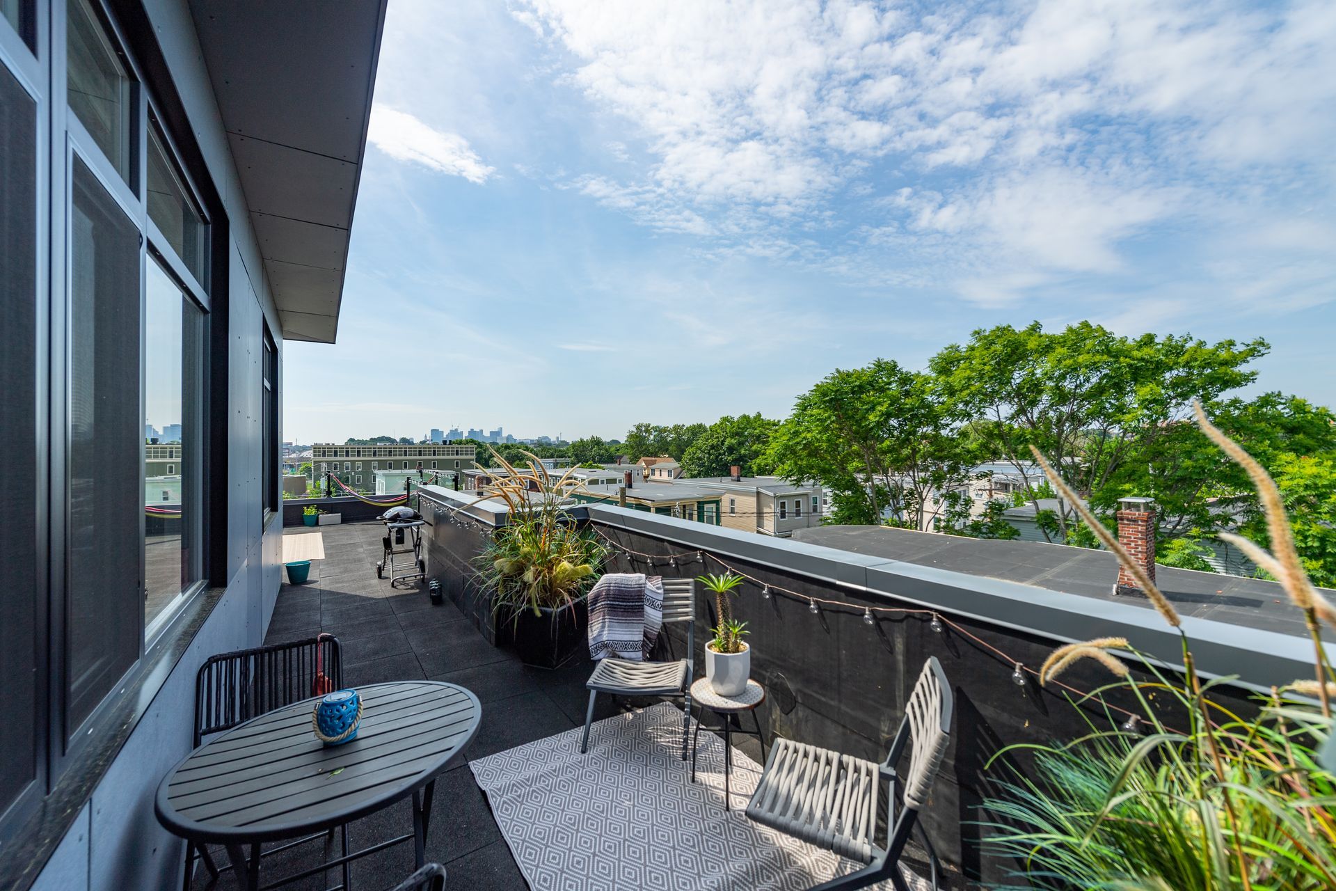 Rooftop patio with seating, plants, and a city view on a sunny day.