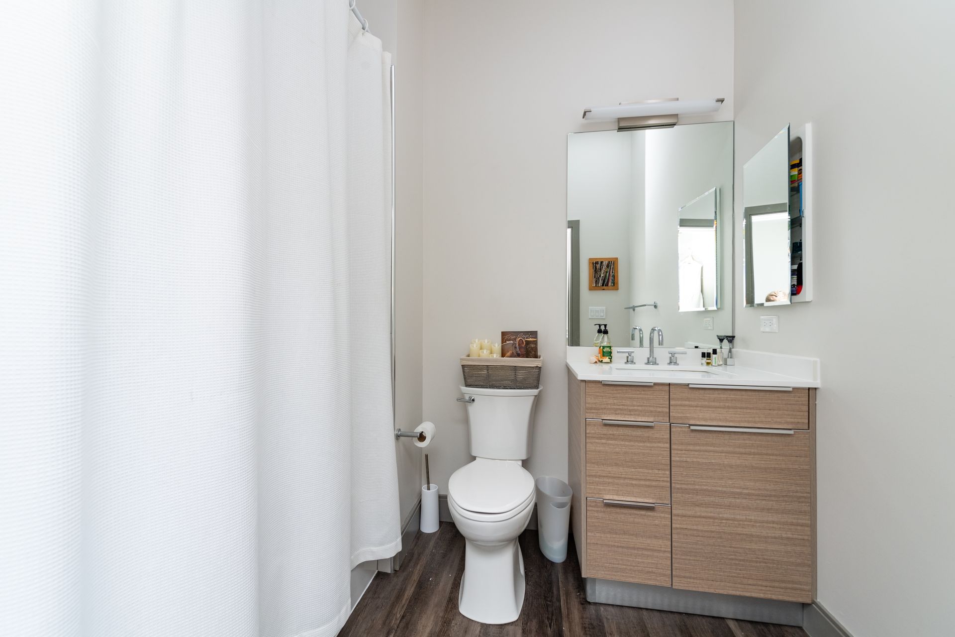 Bathroom with white walls, shower curtain, and a wooden vanity.
