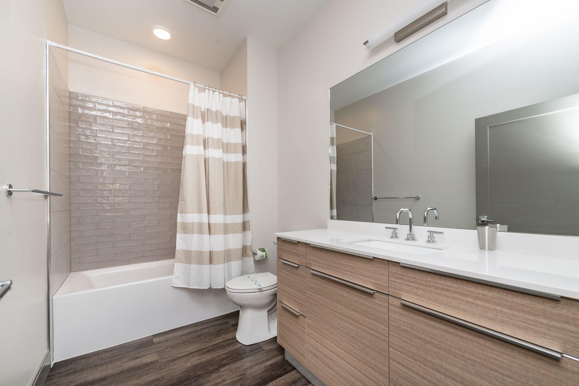 Bathroom with white tub, tan vanity, large mirror, and neutral-toned shower curtain.