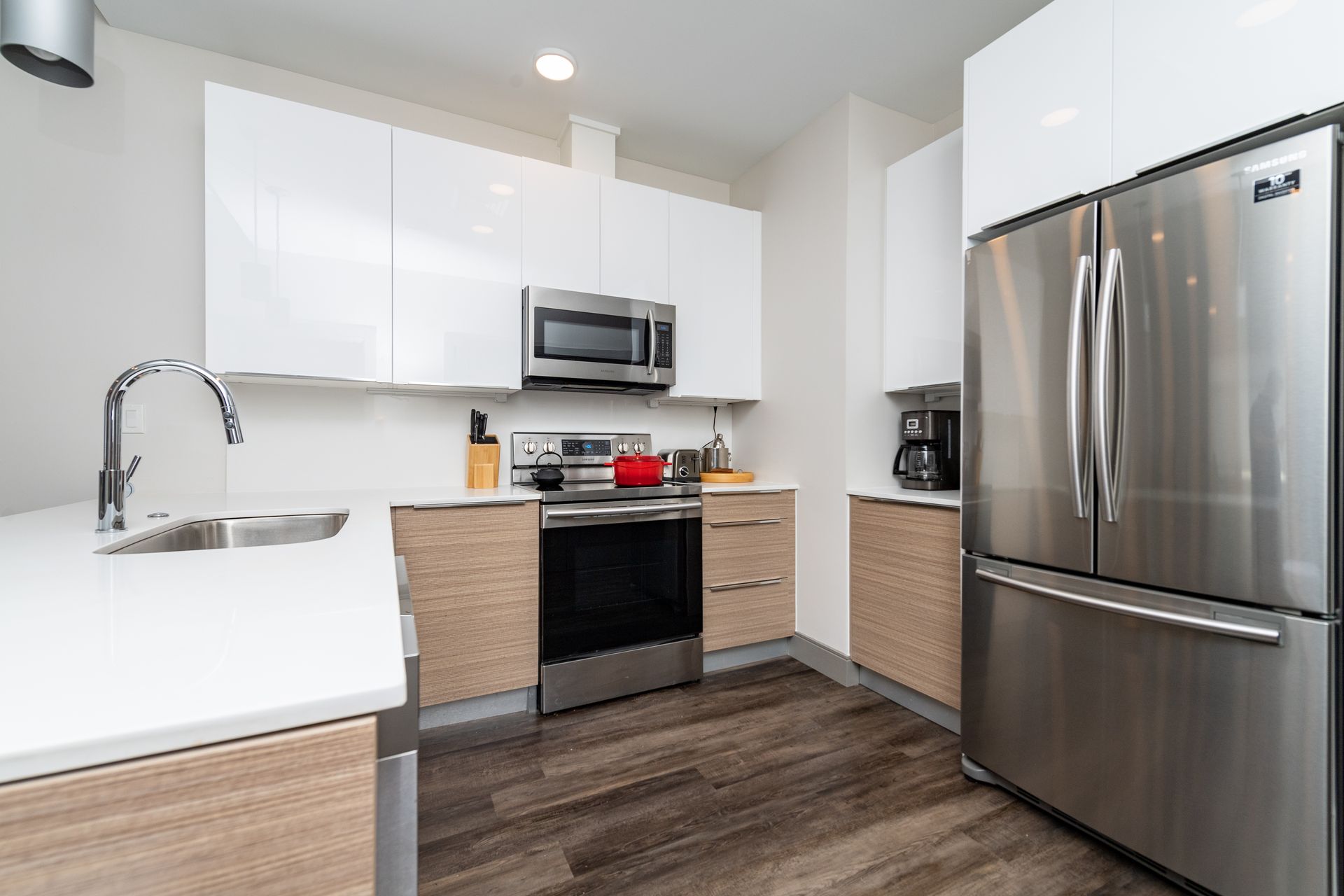 Modern kitchen with white and wood cabinets, stainless steel appliances, and a red pot on the stovetop.