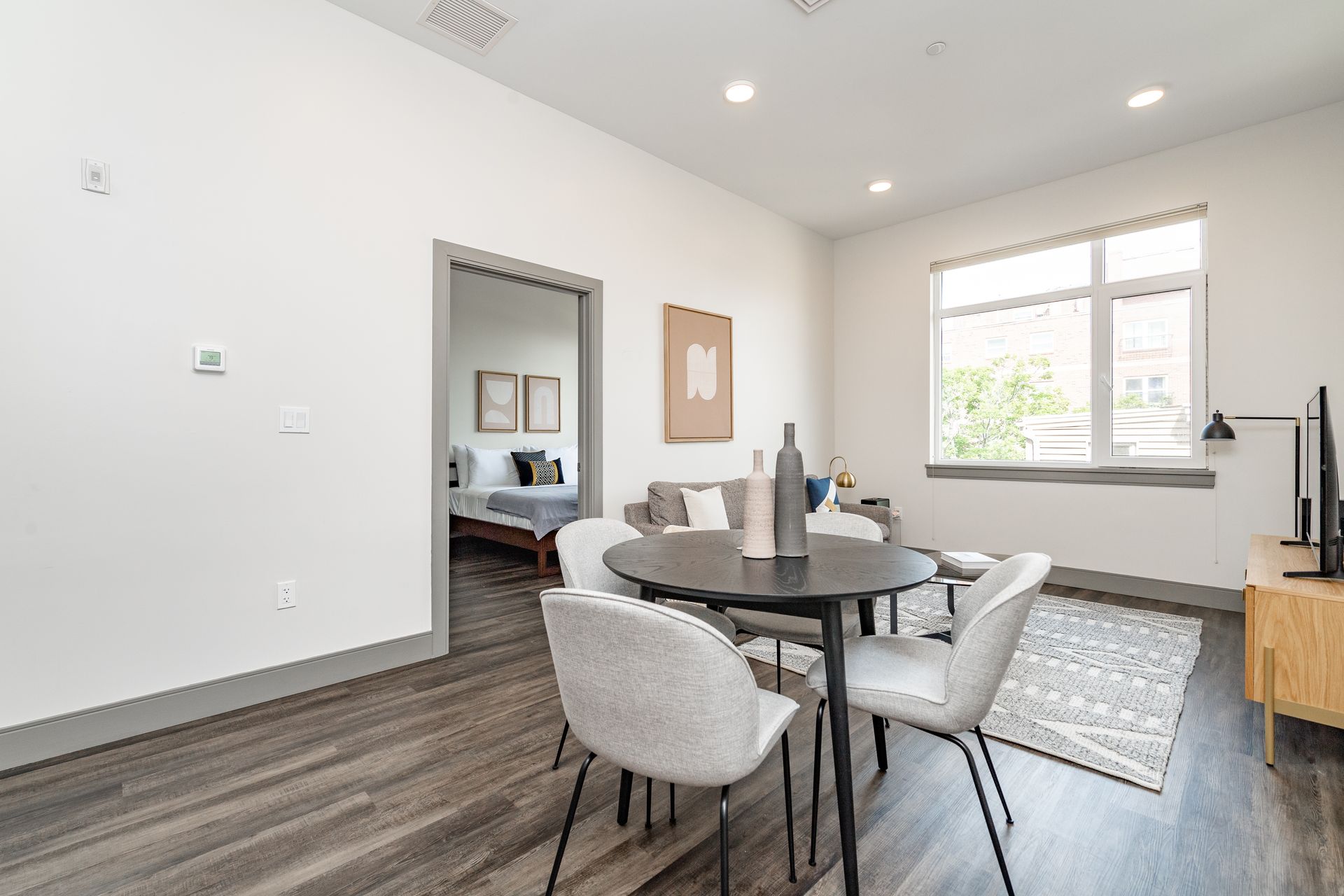 Living room with a dark round table and four chairs, and a doorway to a bedroom.