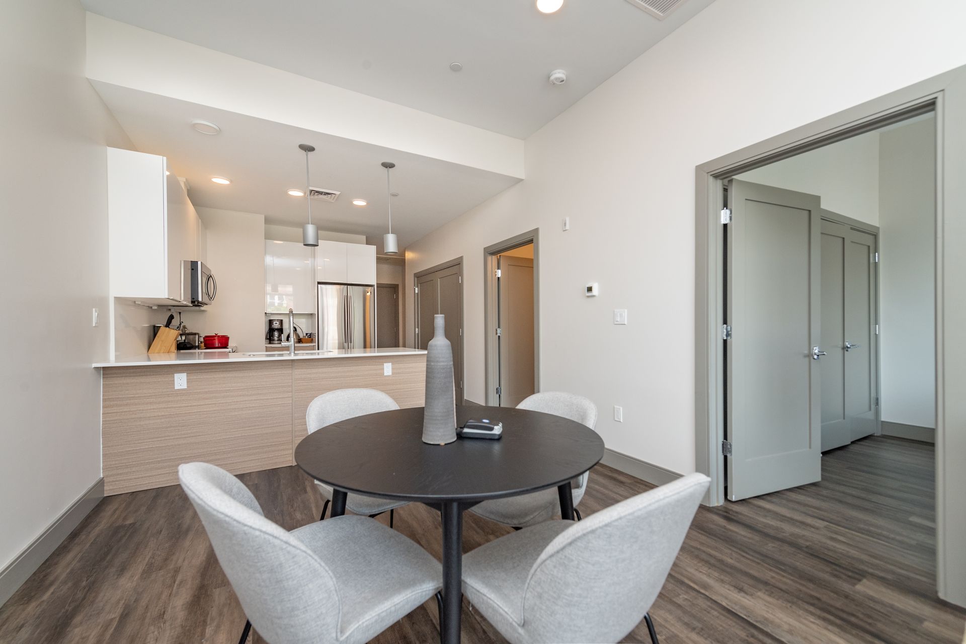 A modern dining area with a round table and four chairs, connected to a kitchen.