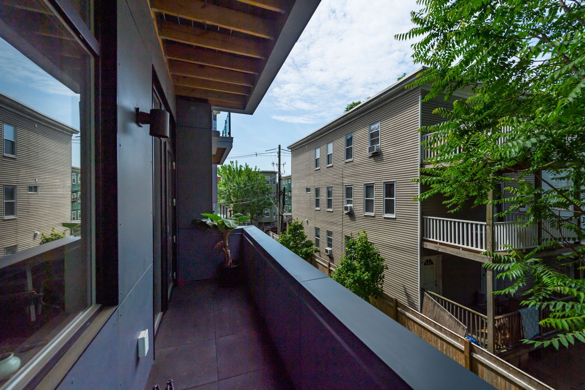 Balcony with dark walls, looking out at a multi-story building and trees under a cloudy sky.