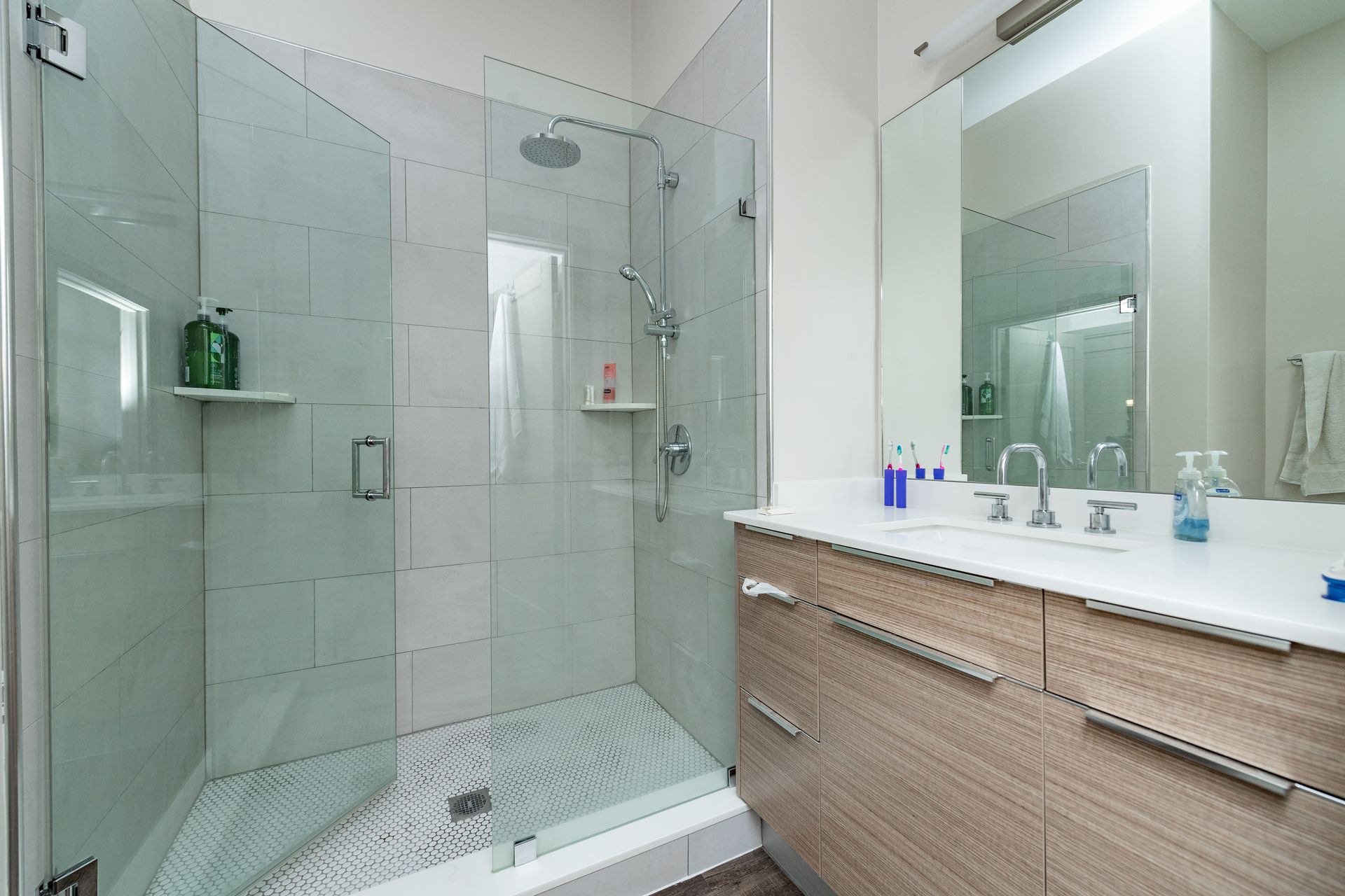 Modern bathroom with glass shower, light wood vanity, and large mirror.