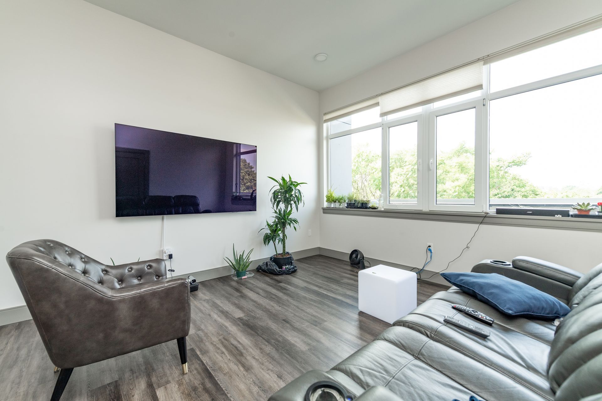 Living room with large TV, gray flooring, window, and leather furniture.
