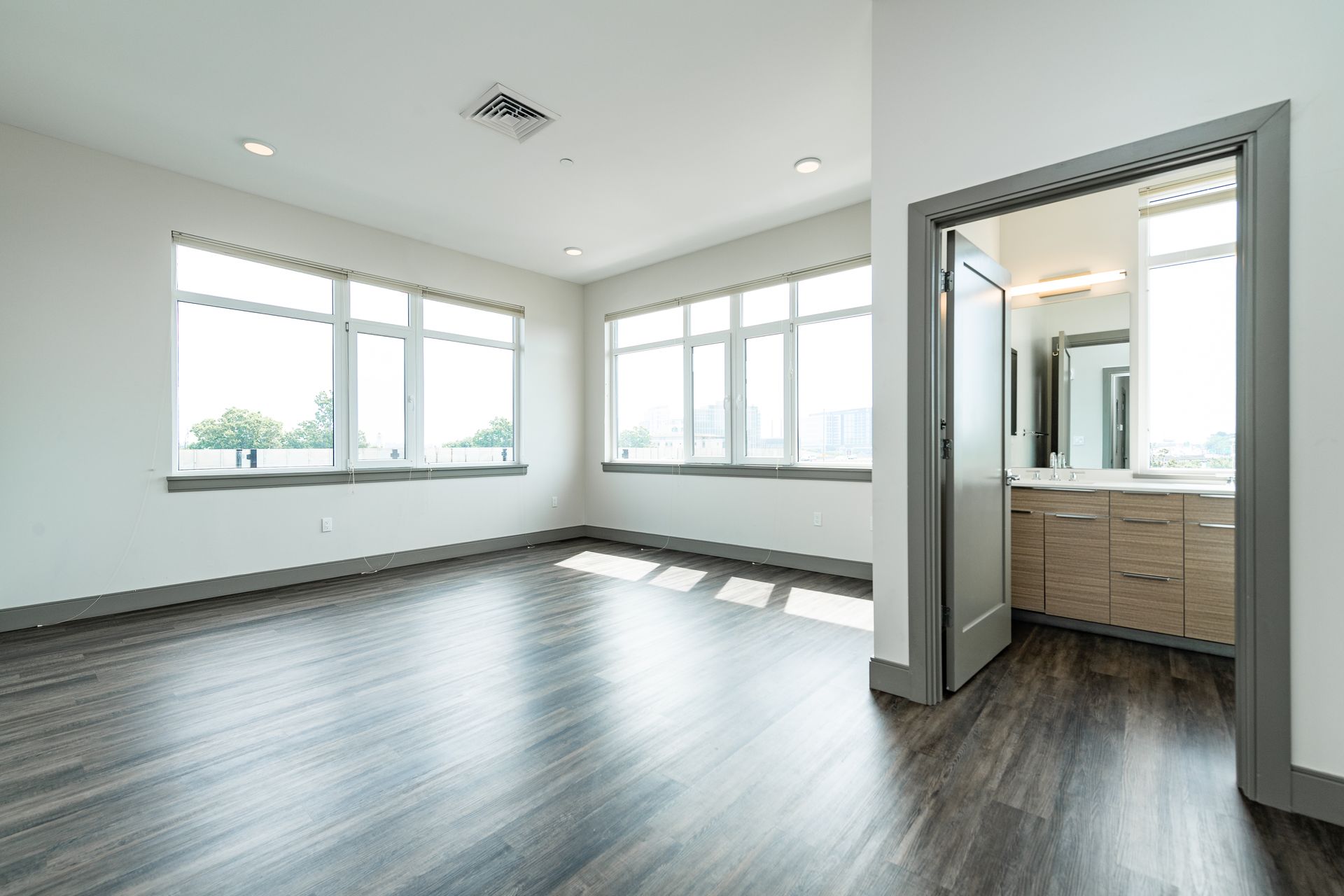Empty room with hardwood floors, large windows, and an open doorway leading to a bathroom.