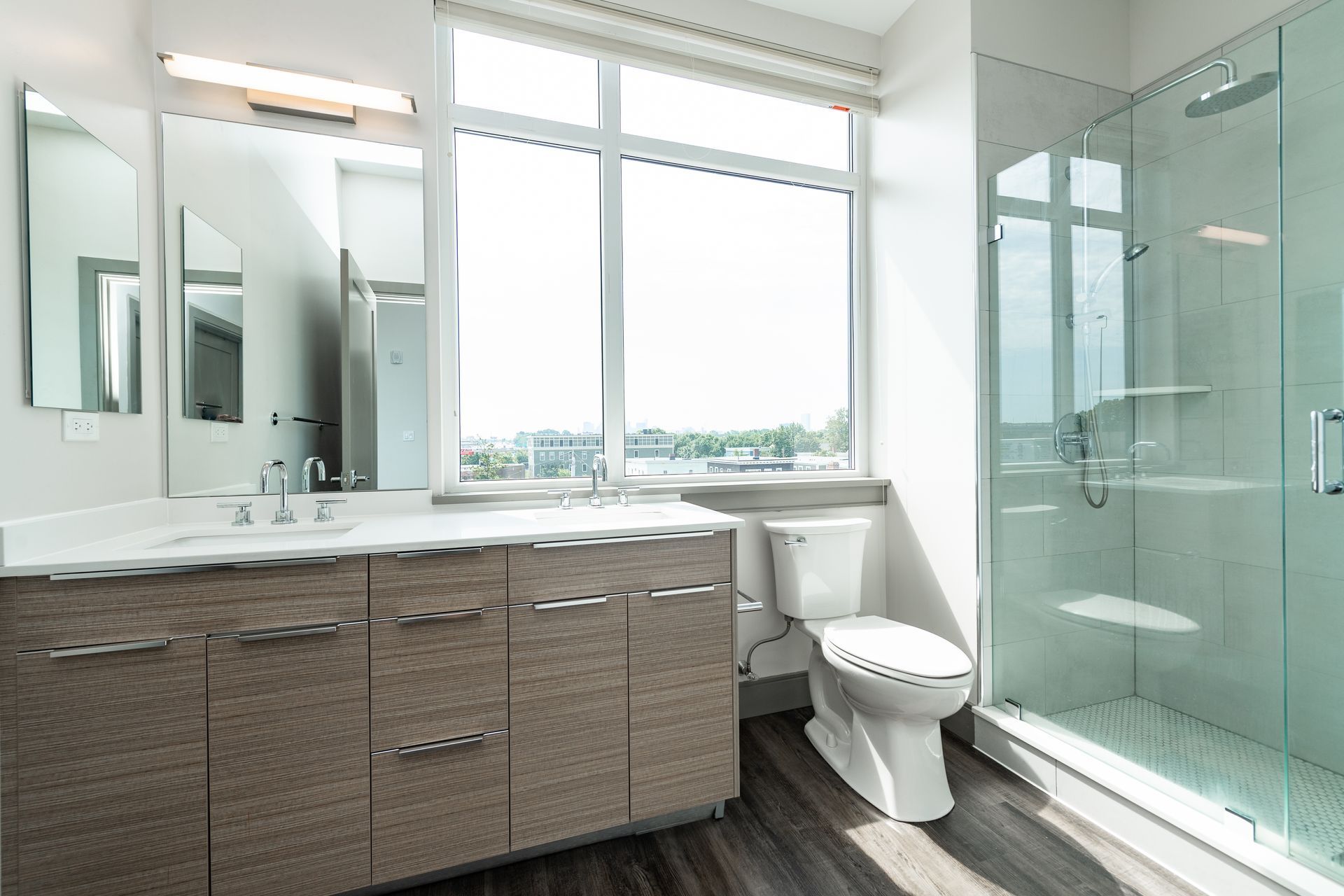 Modern bathroom with a large window, vanity, toilet, and glass shower.