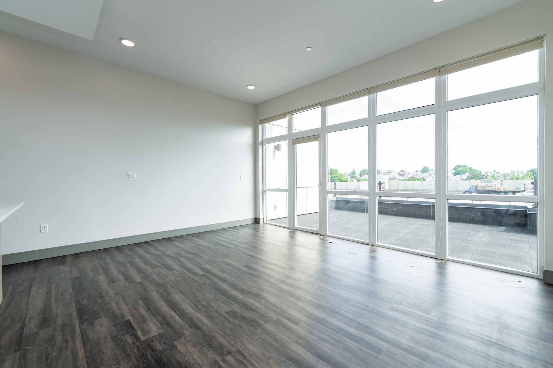 Empty room with large windows, dark wood flooring, and white walls.