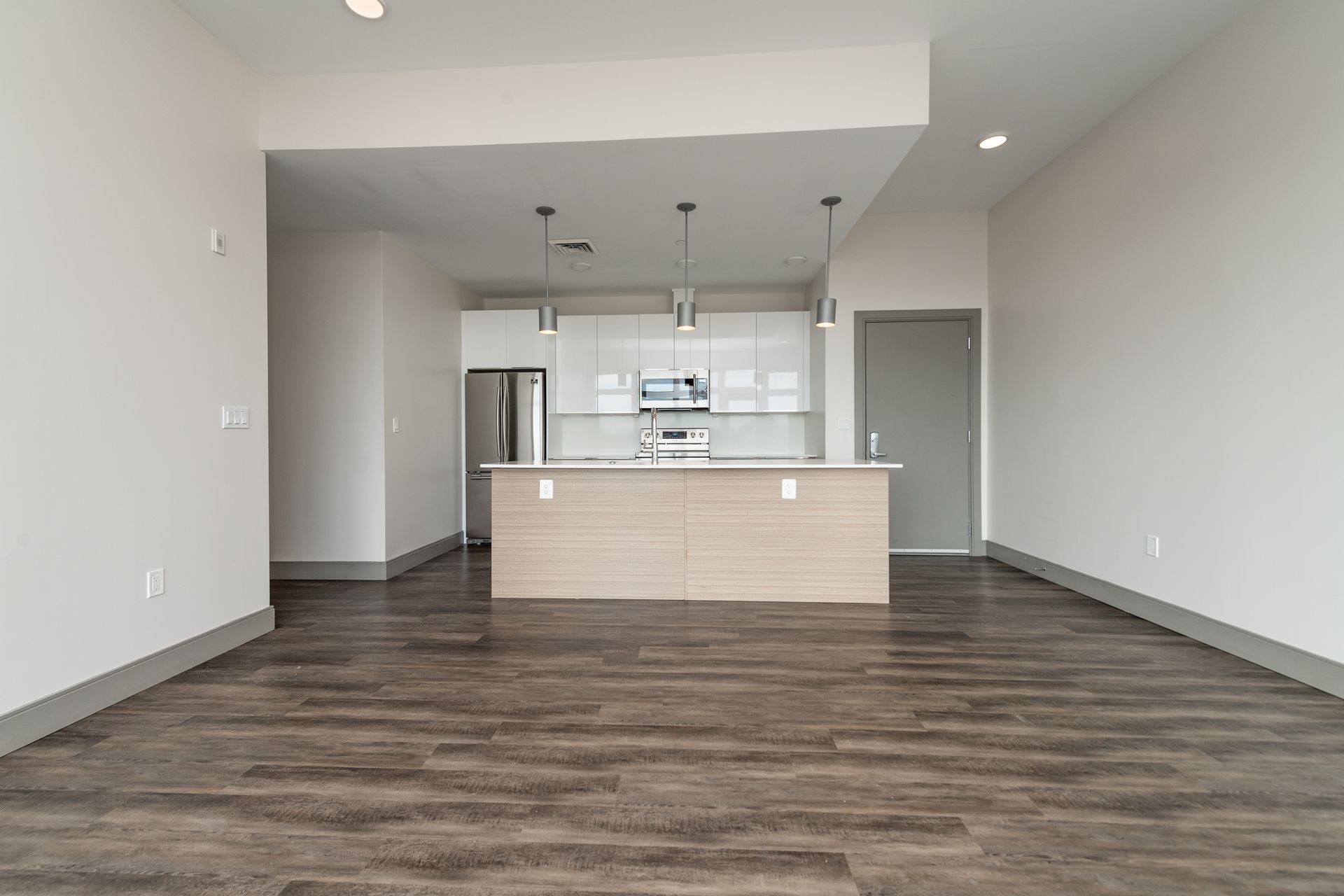 Modern apartment interior with kitchen island, stainless steel appliances, and wood-look flooring.