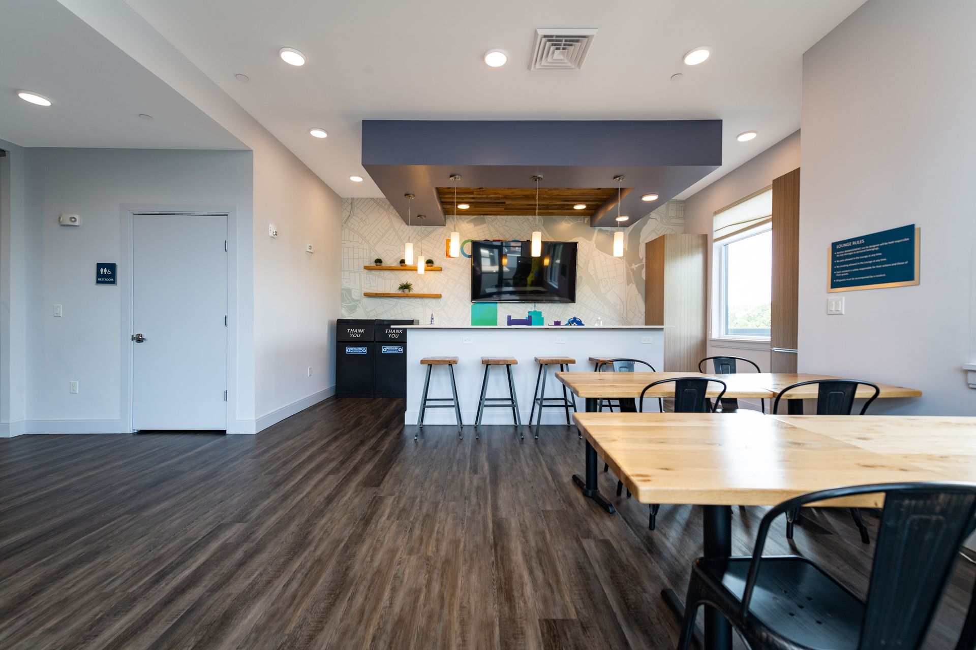 Modern common area with tables, bar seating, TV, and light wood floors.