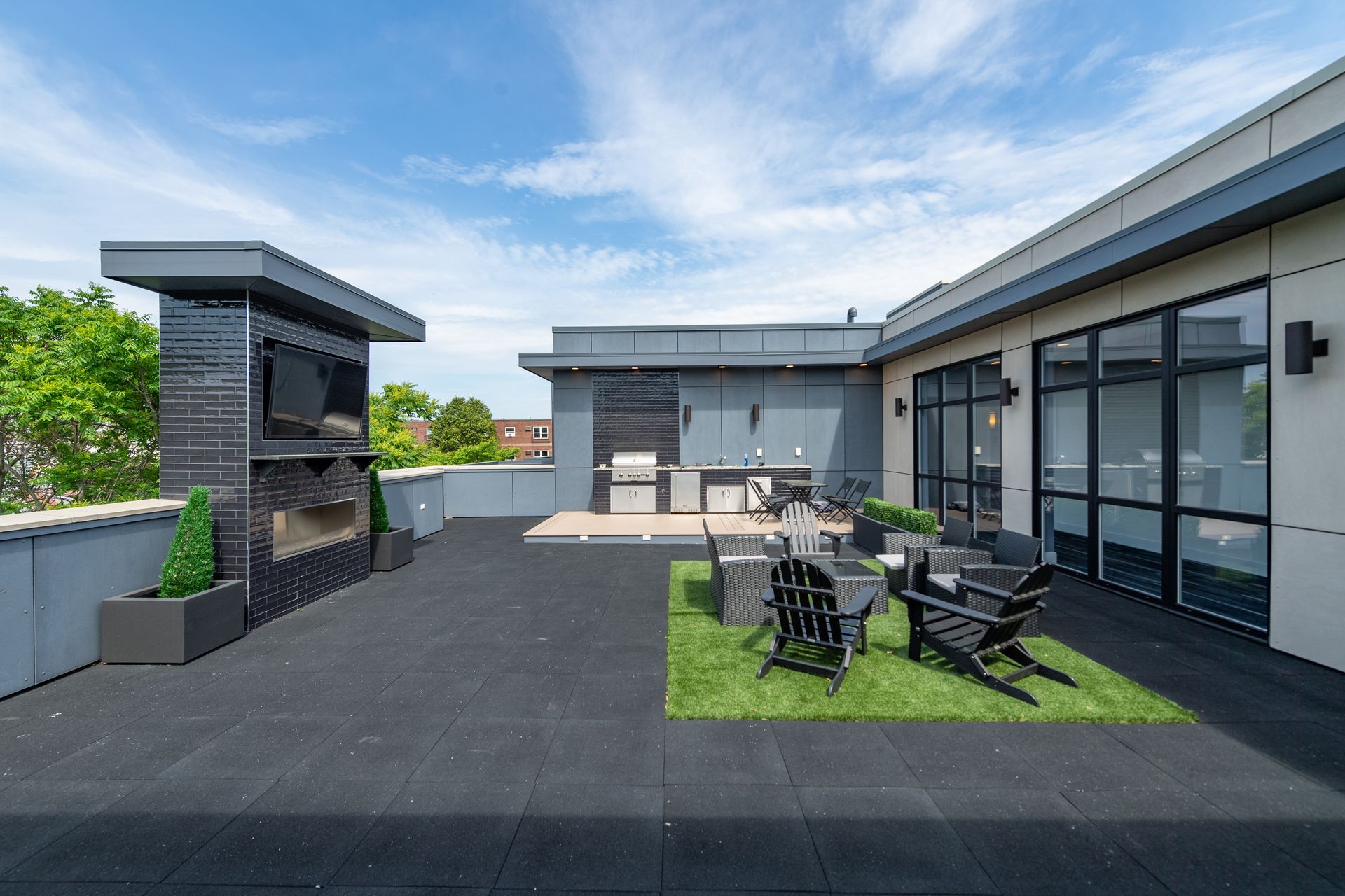 Rooftop patio with fireplace, outdoor kitchen, seating, and faux grass patch; bright sky.